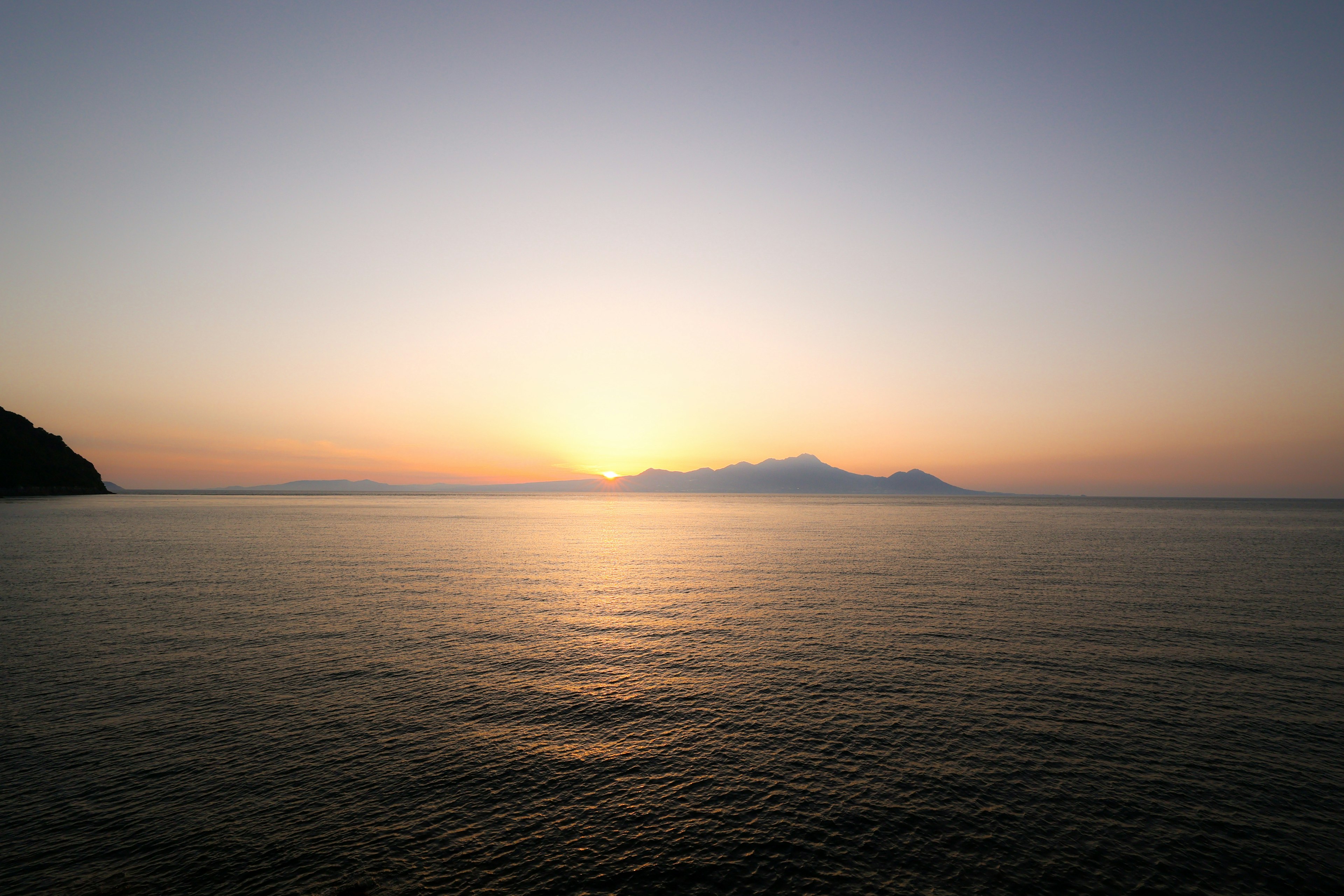 穏やかな海の向こうに沈む夕日と遠くの島々