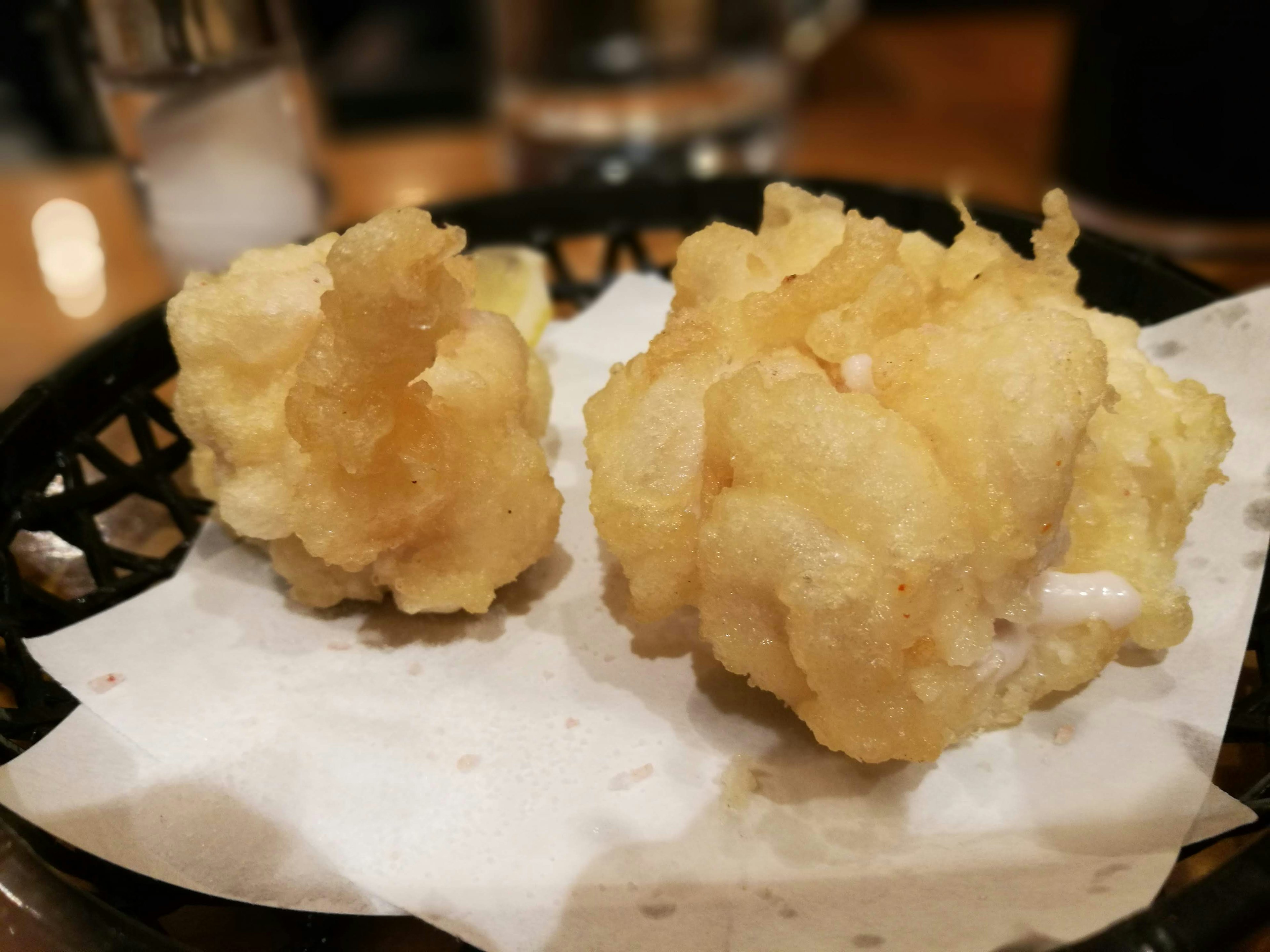 Hai miếng tempura vàng với kết cấu giòn được phục vụ trên đĩa có lót giấy