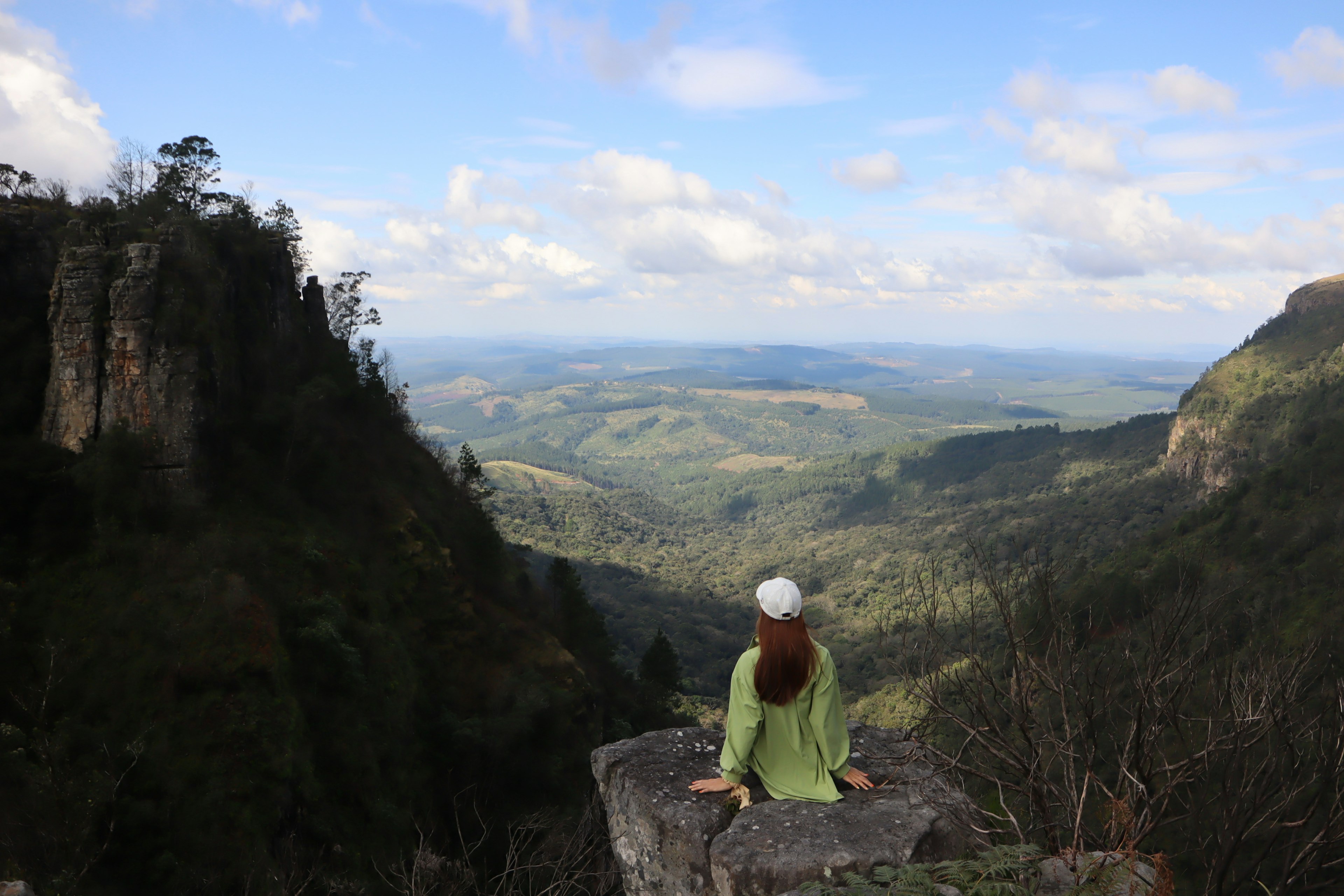 Mujer con atuendo verde sentada en una roca mirando un vasto paisaje montañoso