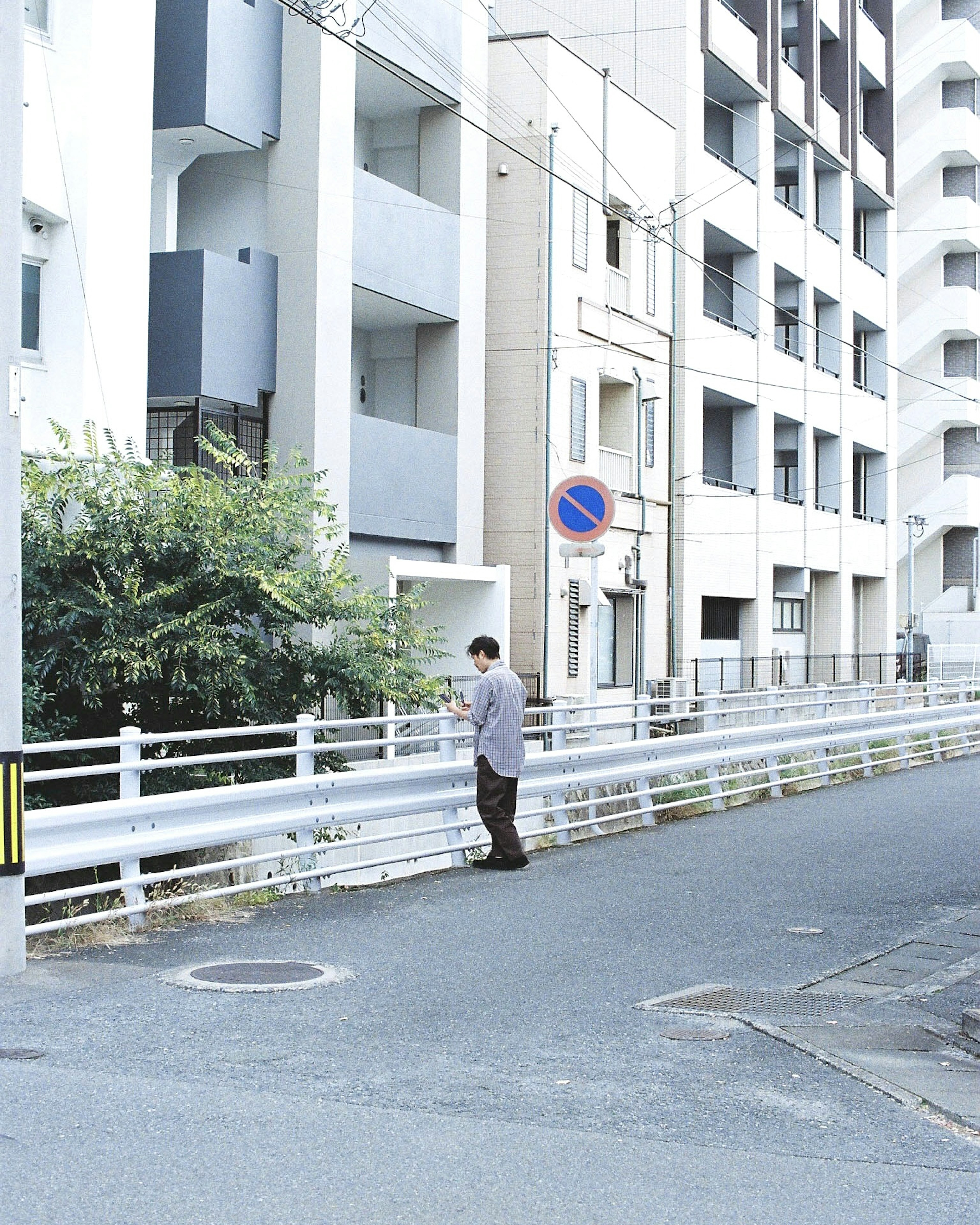 住宅街の白いフェンスの前に立つ男性と近くの建物