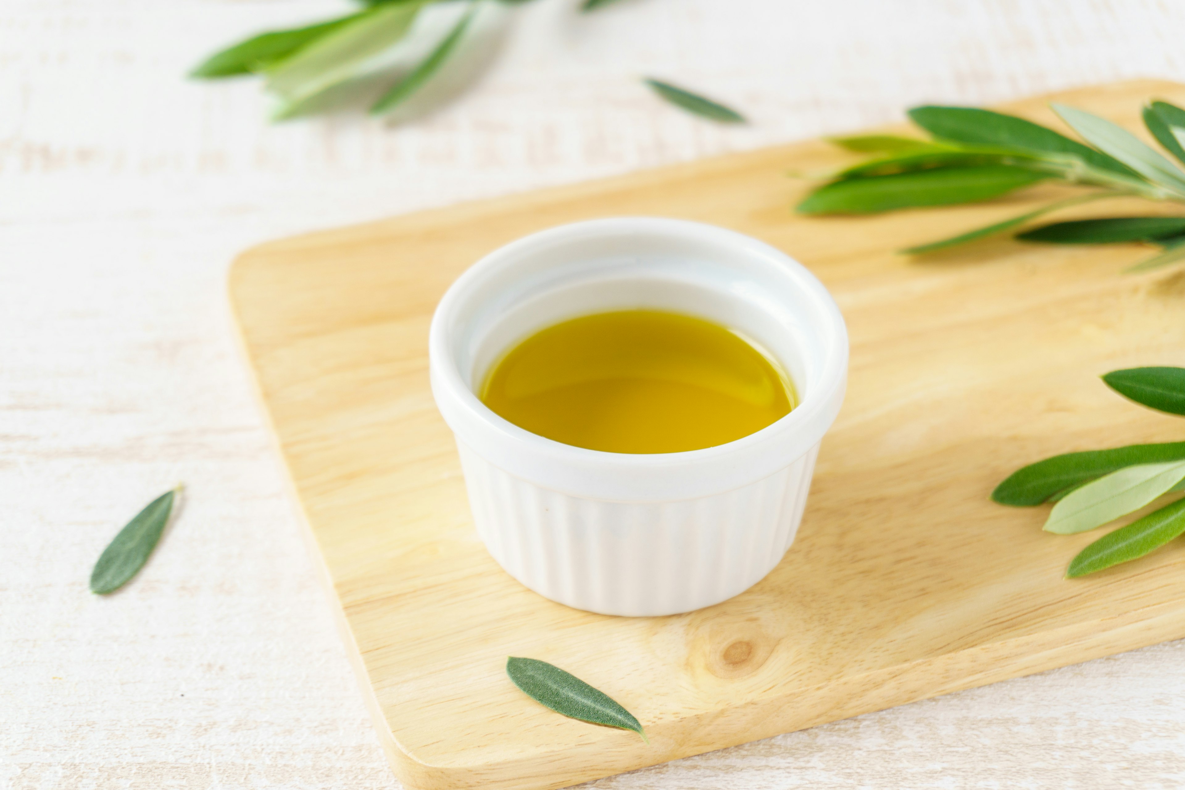 Un petit bol blanc avec de l'huile d'olive sur une planche en bois entouré de feuilles d'olive