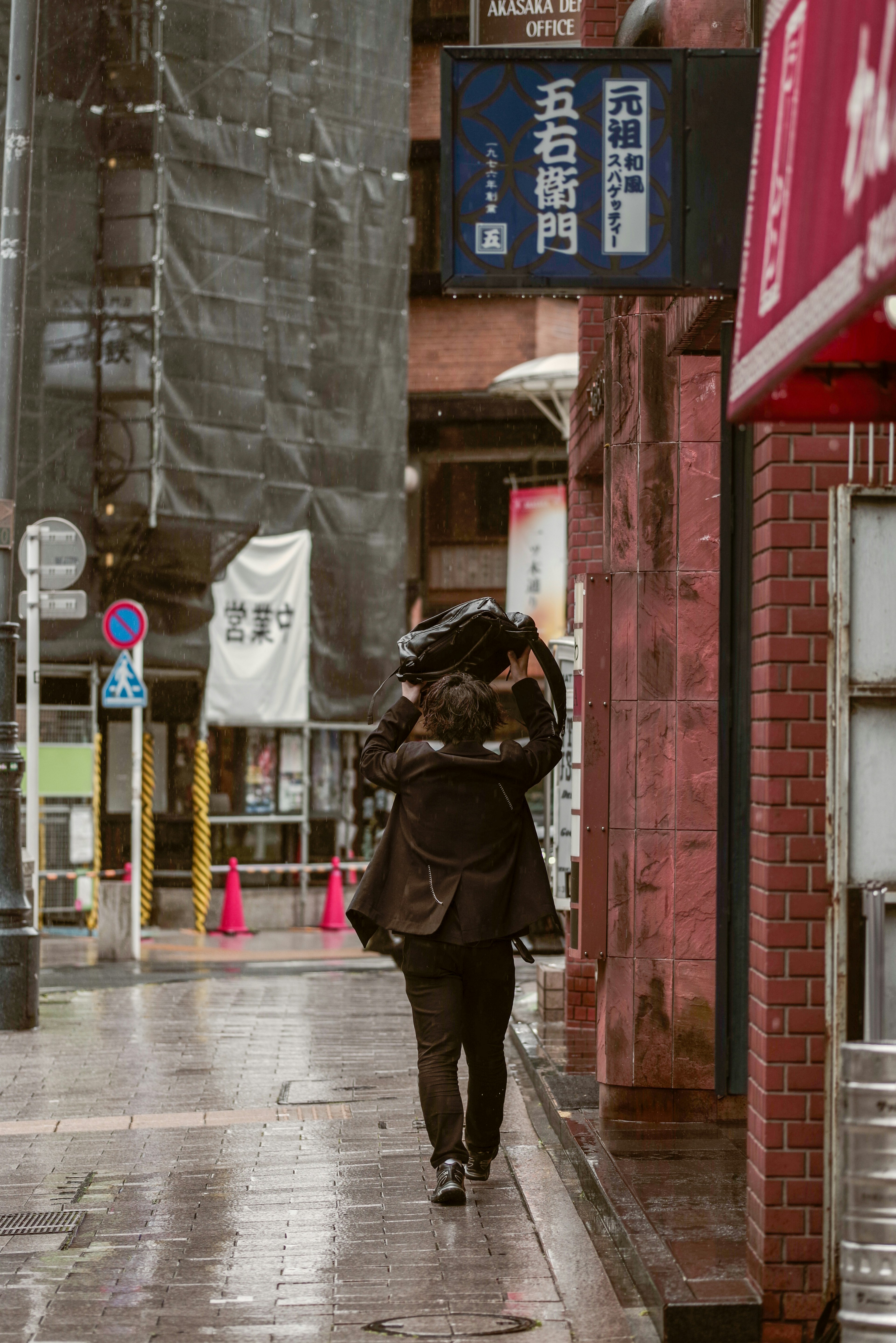 Una persona caminando bajo la lluvia llevando una bolsa en la espalda en una calle de la ciudad
