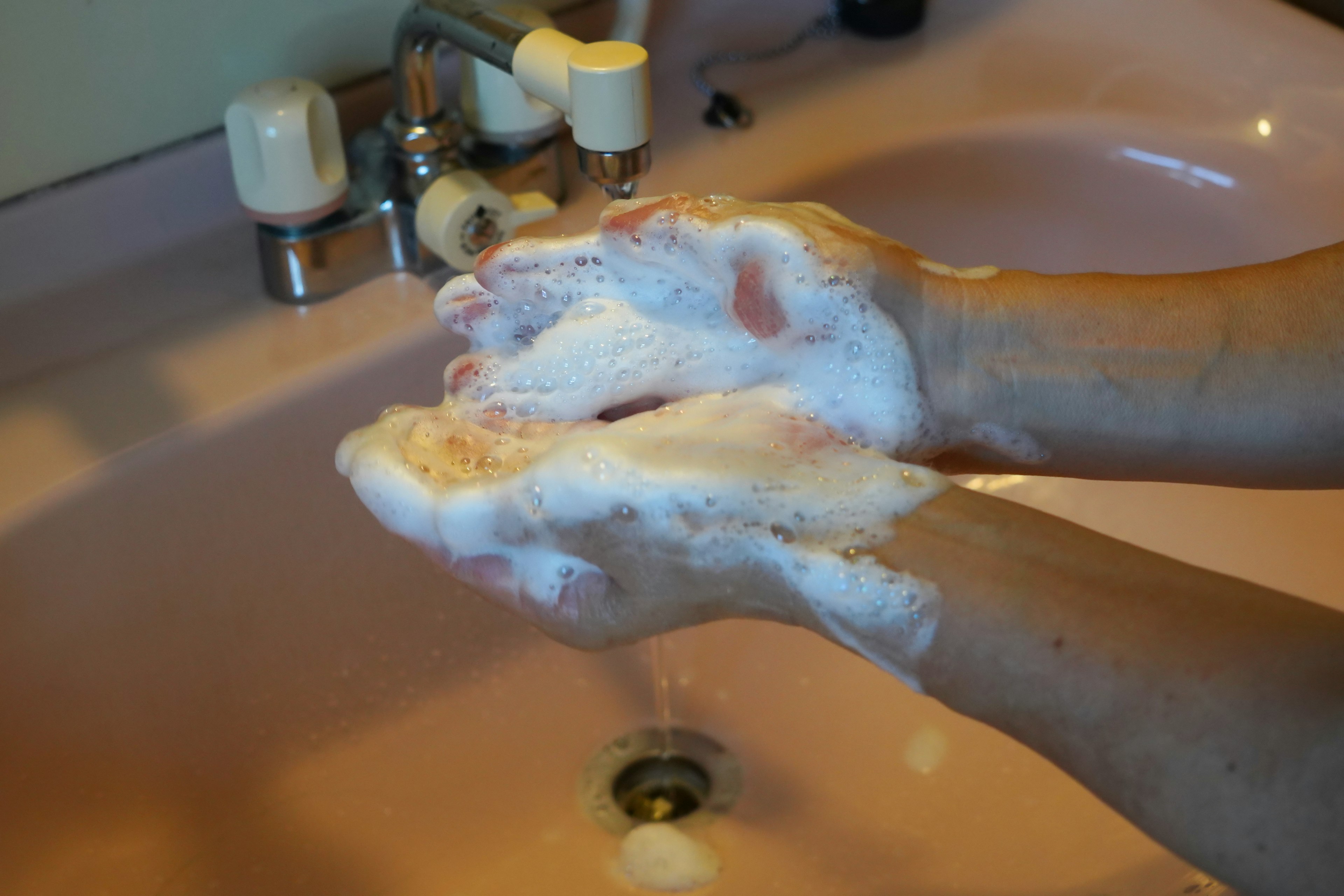 Hands lathered with soap at a pink sink