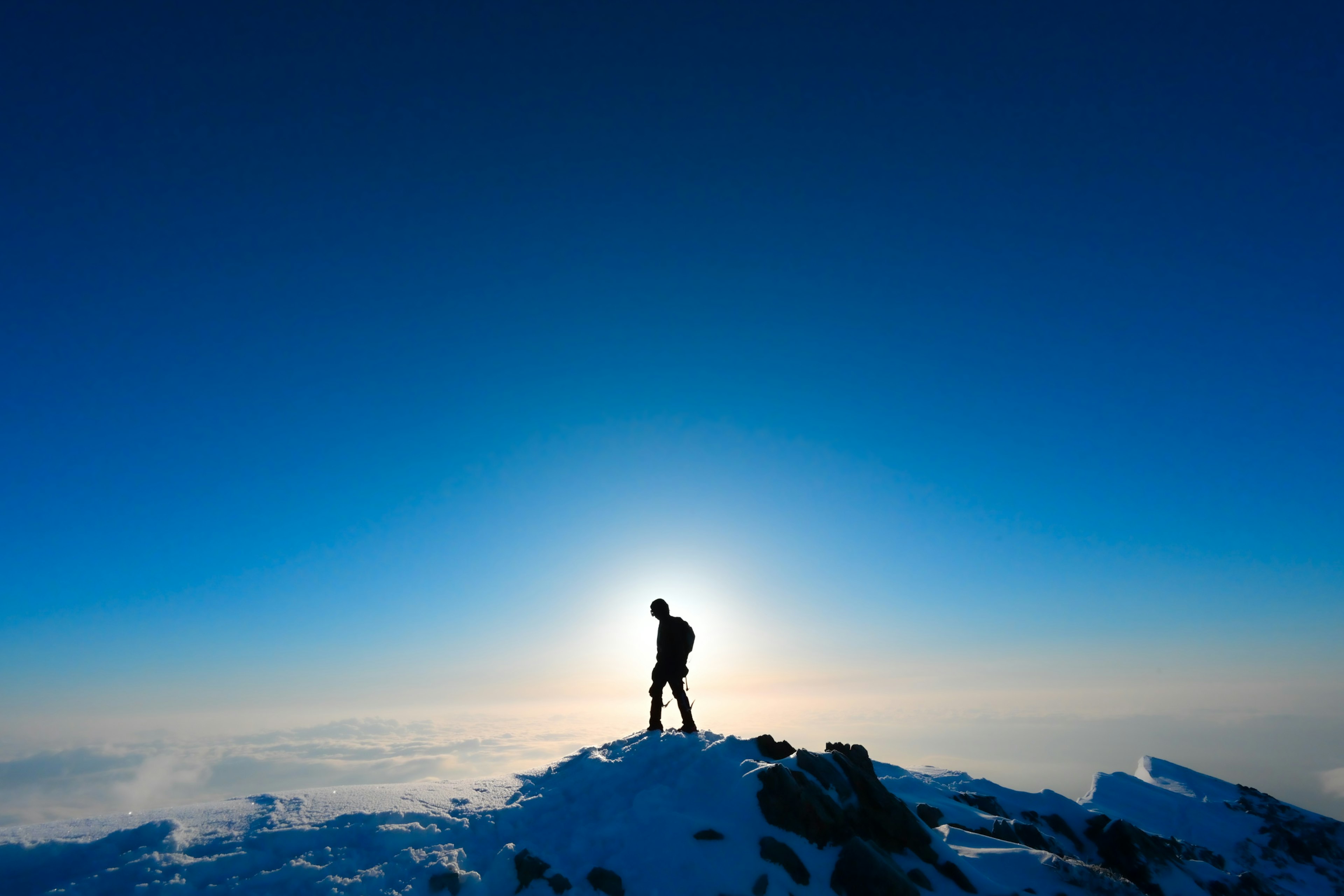 Silhouette d'un randonneur se tenant au sommet d'une montagne enneigée sous un ciel bleu