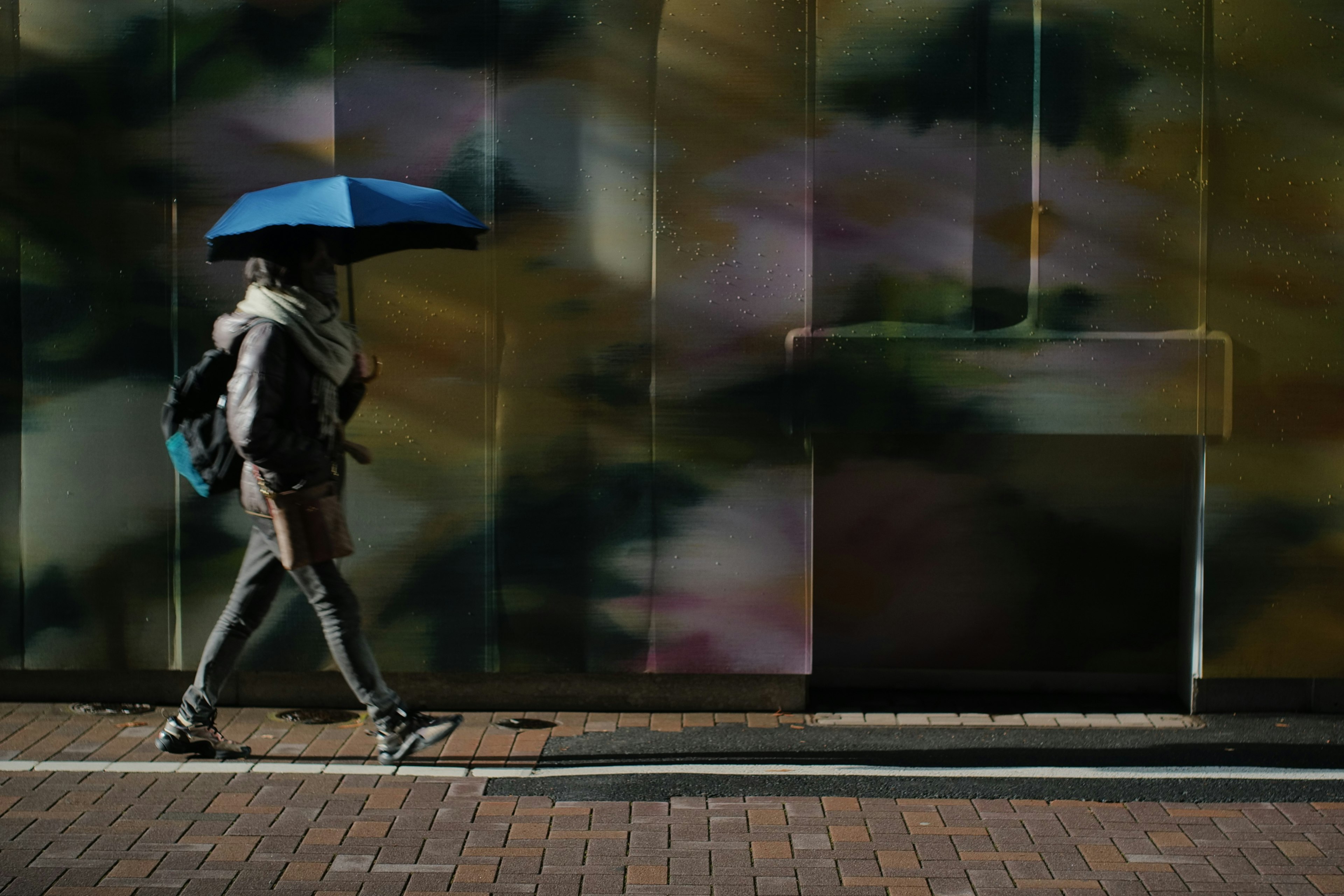 Person walking with a blue umbrella against a colorful wall background