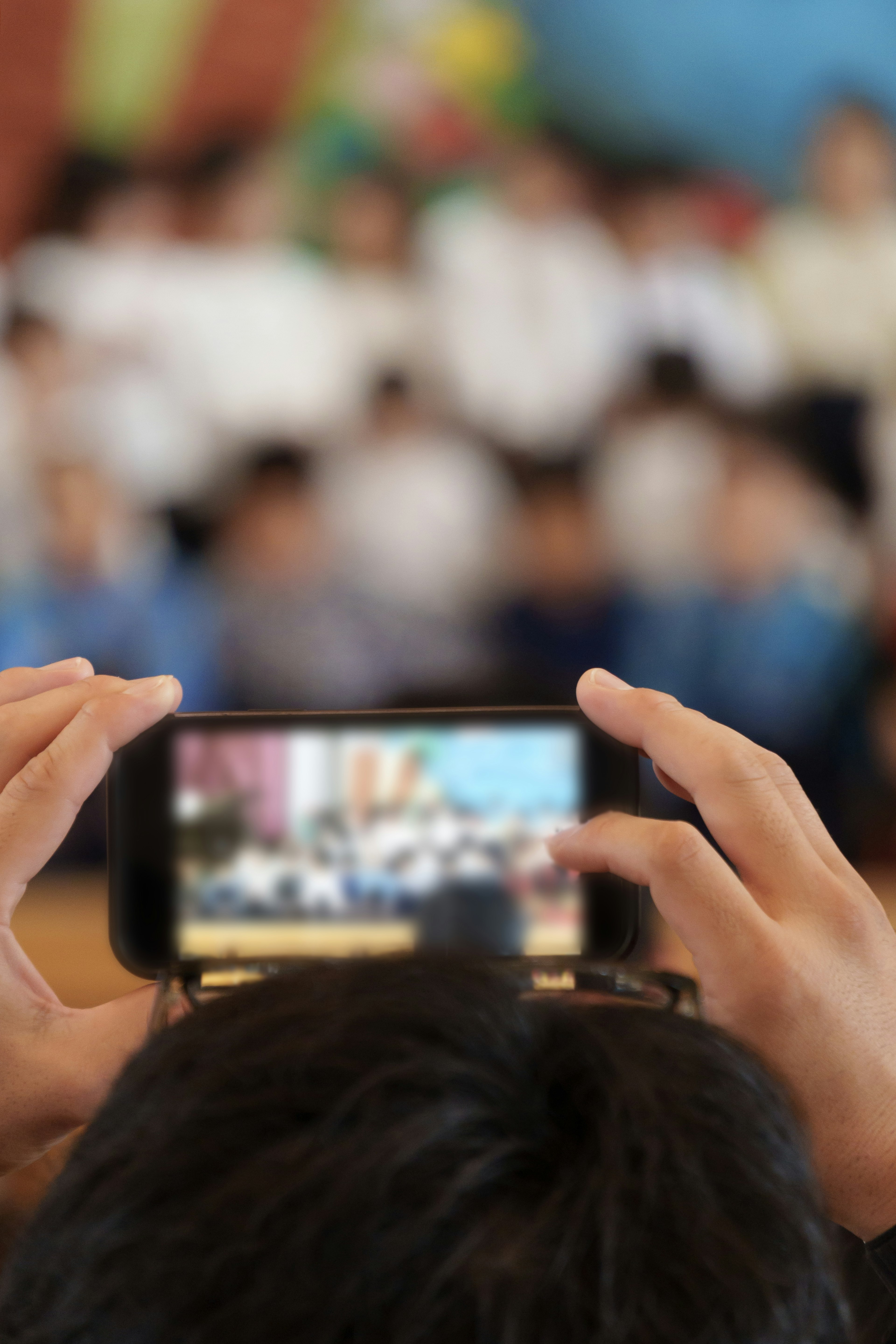 Hands holding a smartphone capturing a blurred group of children in the background