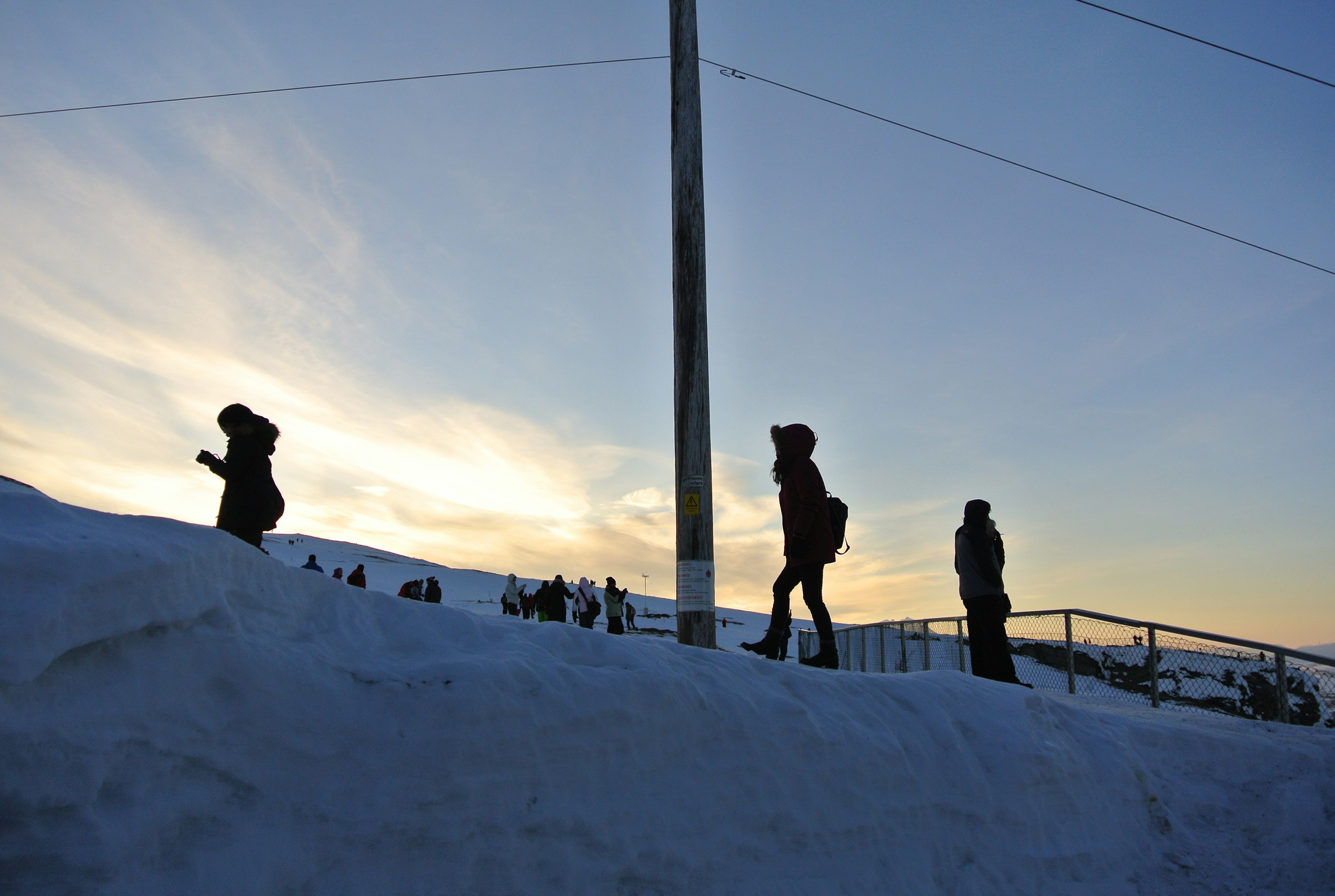 Silhouette di persone che camminano nella neve contro un cielo al tramonto