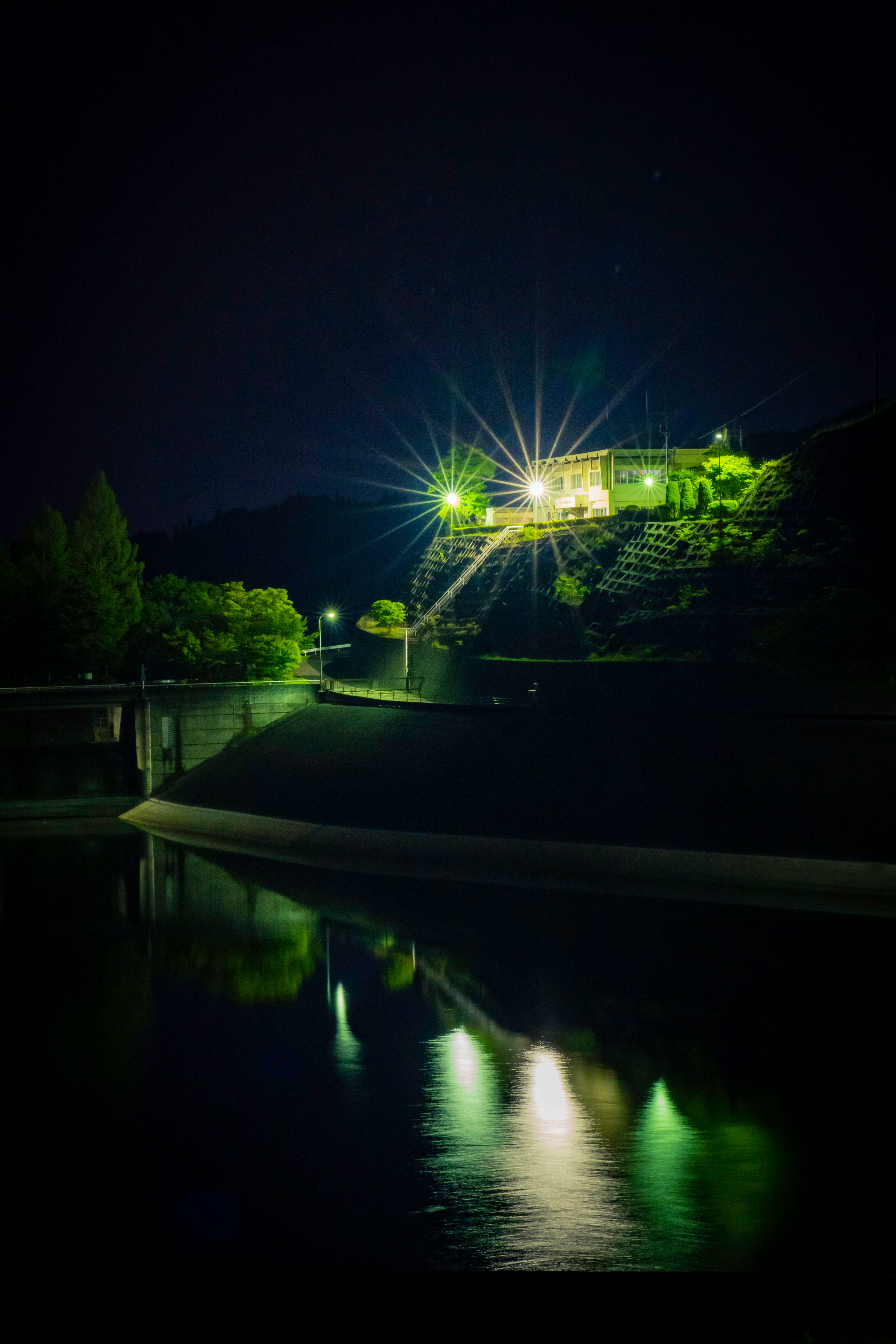 夜の川沿いに立つ明るい家とその反射