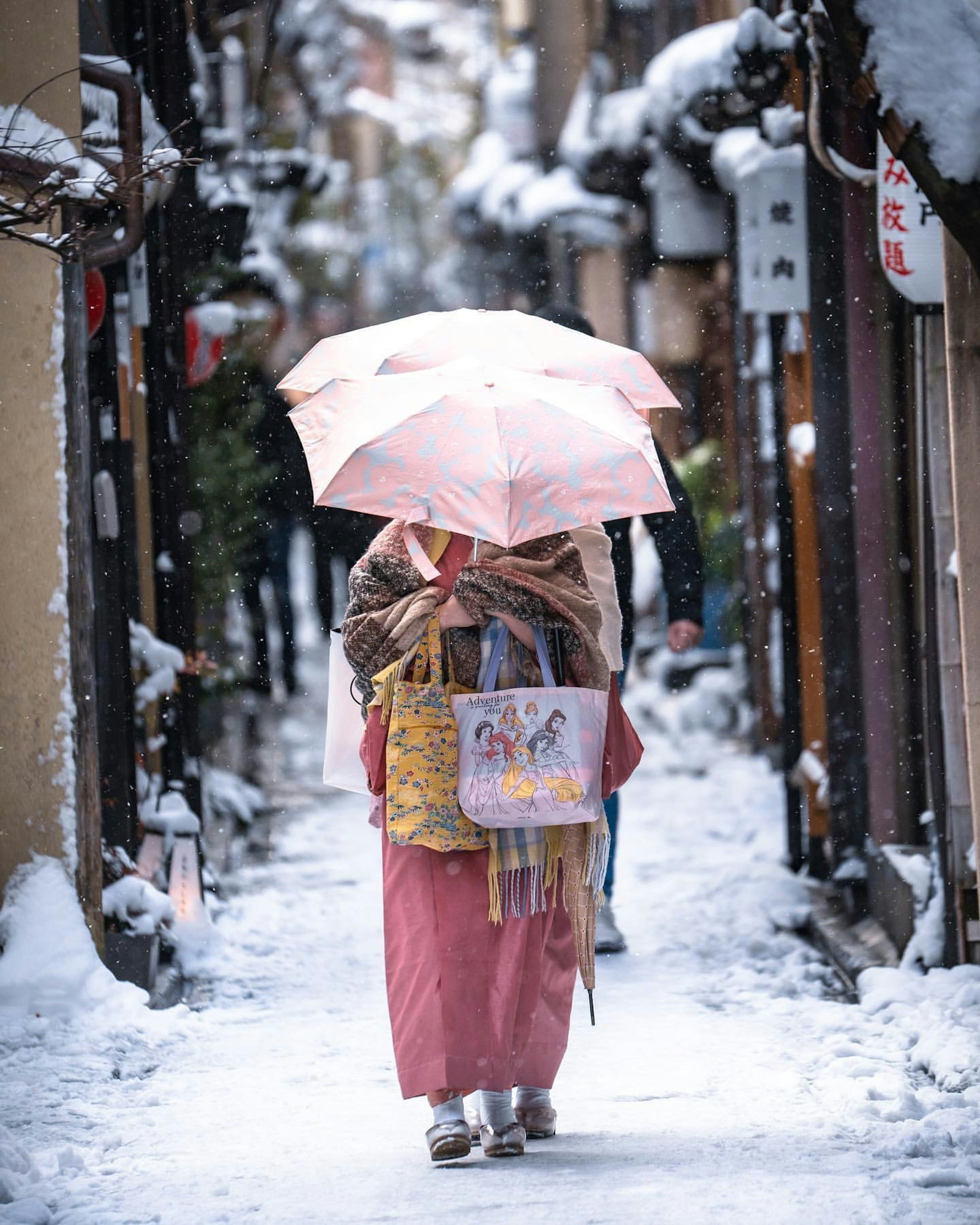 雪に覆われた小道を歩く着物姿の女性がピンクの傘を持っている