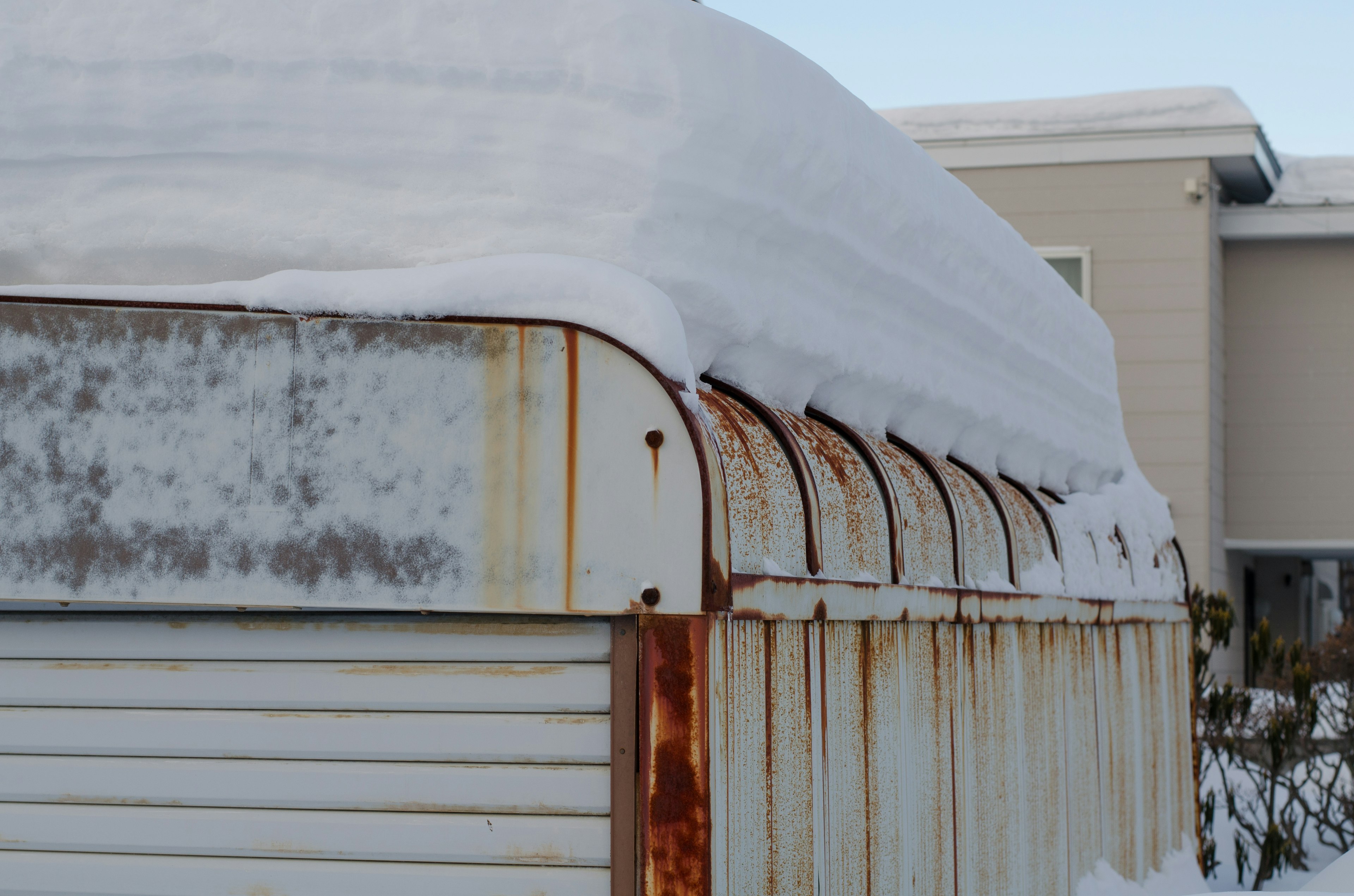 Snow-covered old garage roof with rusty metal side