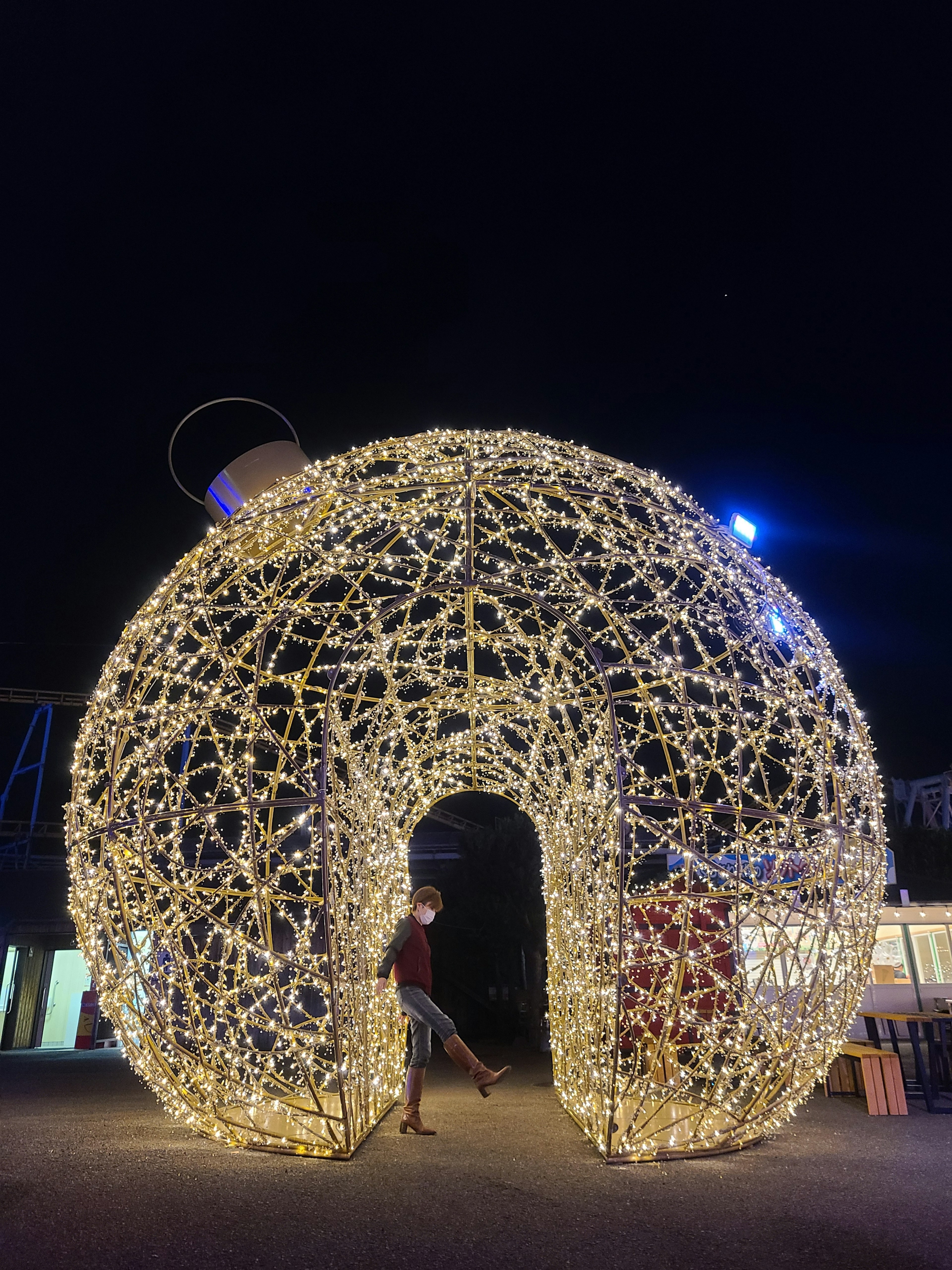 Decorative arch structure illuminated with lights at night with a person standing in front