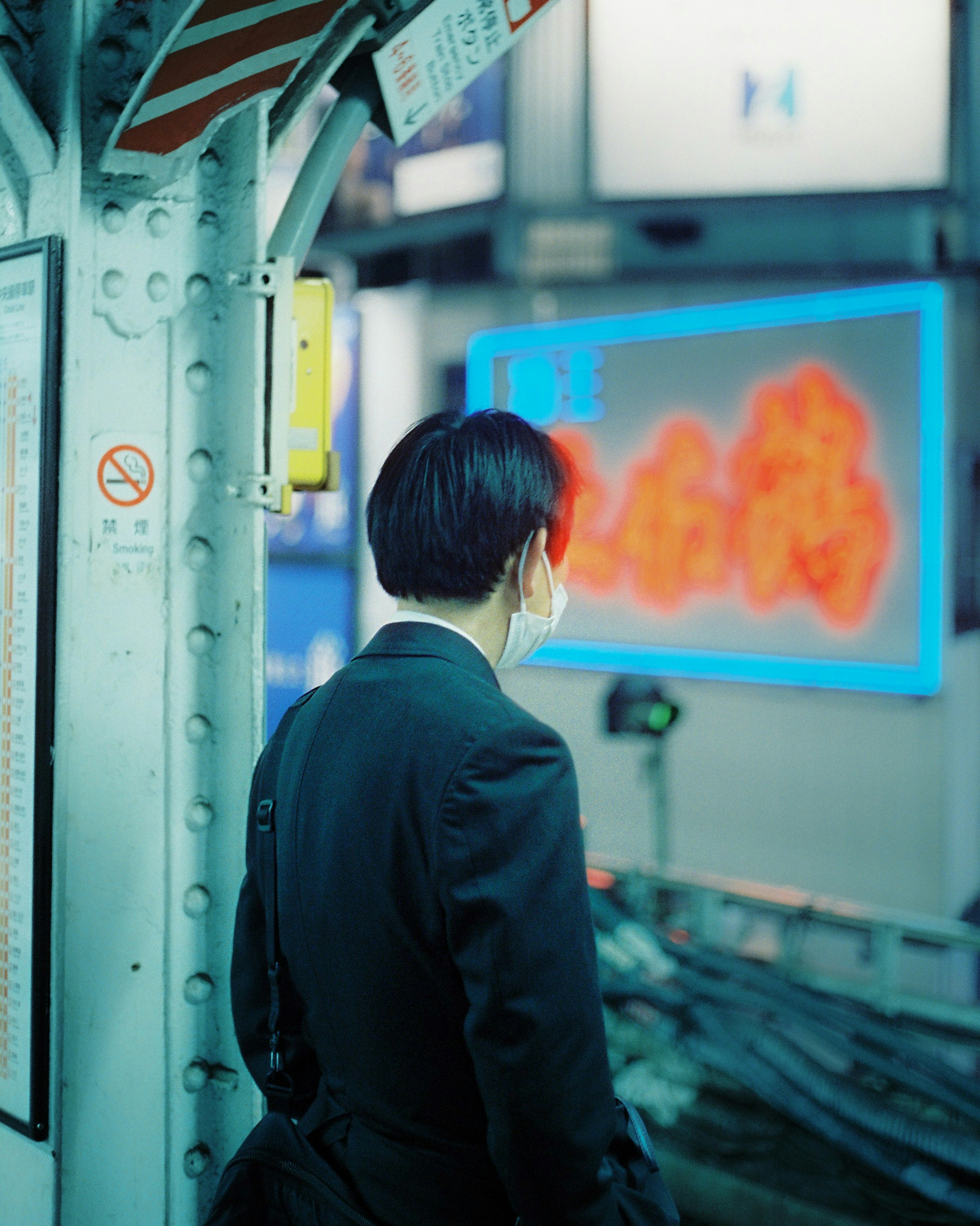 Businessman looking back at a train station platform with a blue neon sign nearby