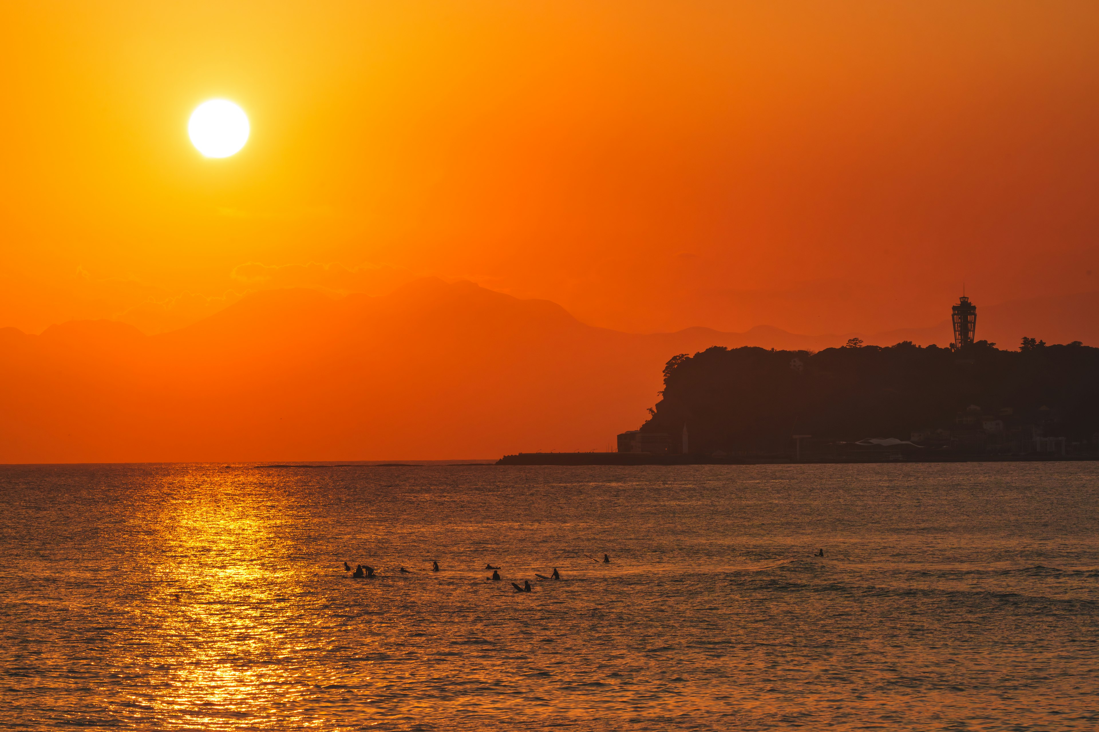 A stunning sunset over the ocean with surfers and a lighthouse in the background