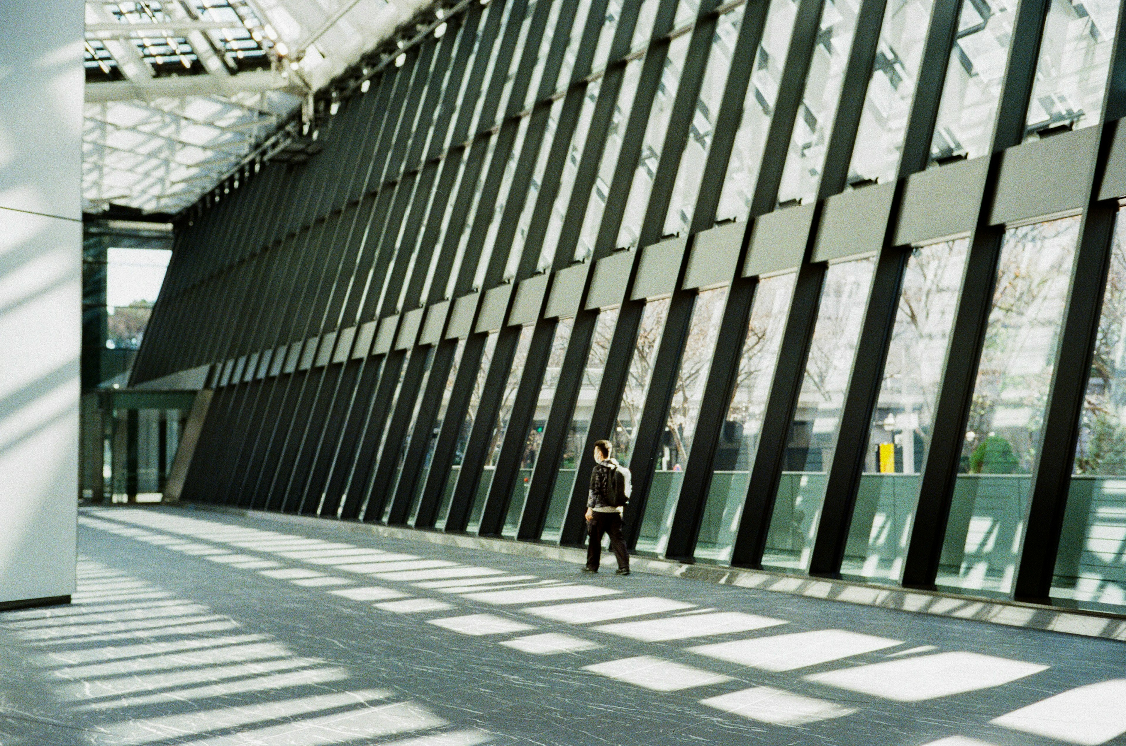 Interior of a modern building Person standing in a spacious area with large windows casting shadows