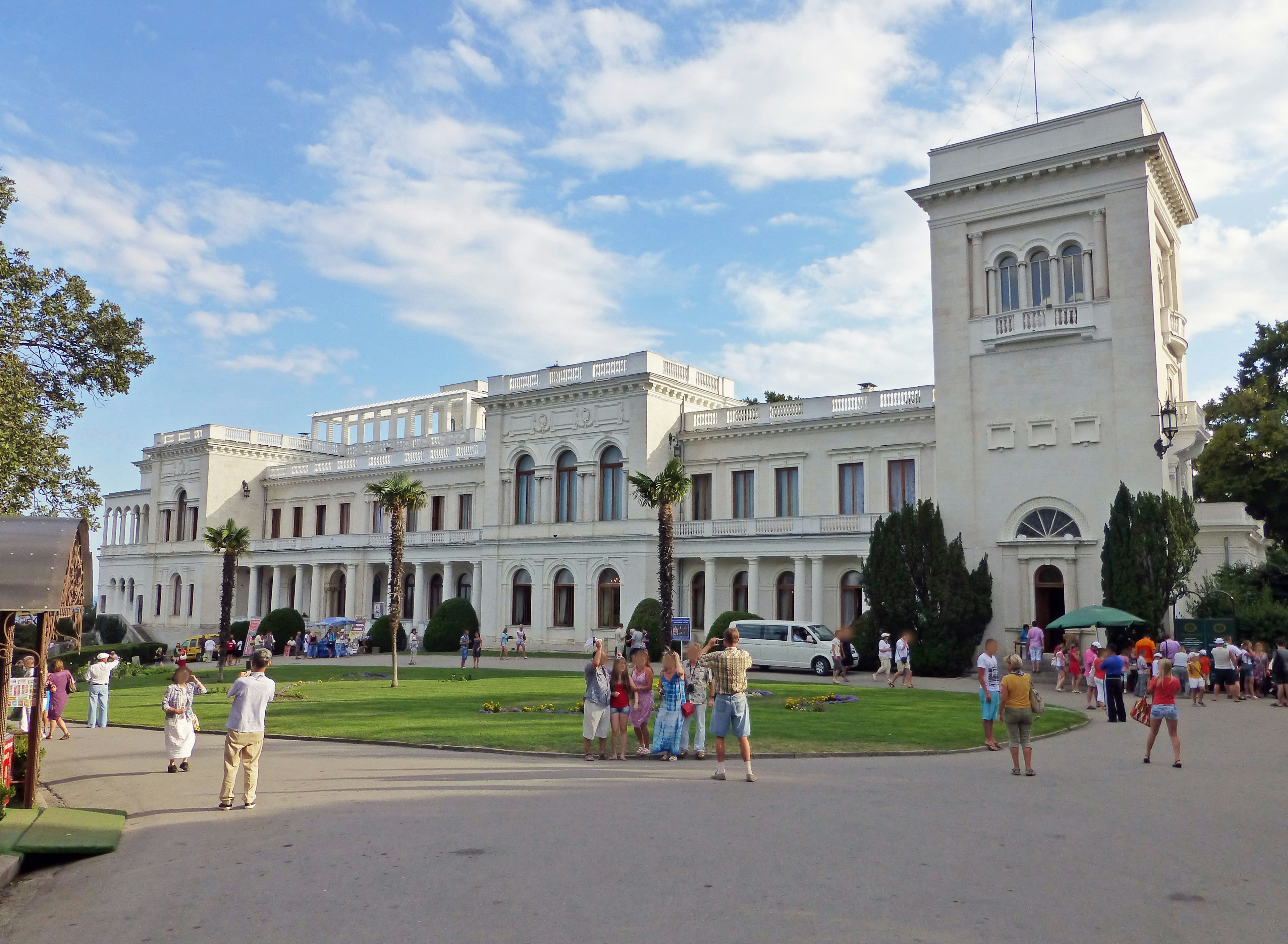 People gathering in a park featuring a white building and green lawn