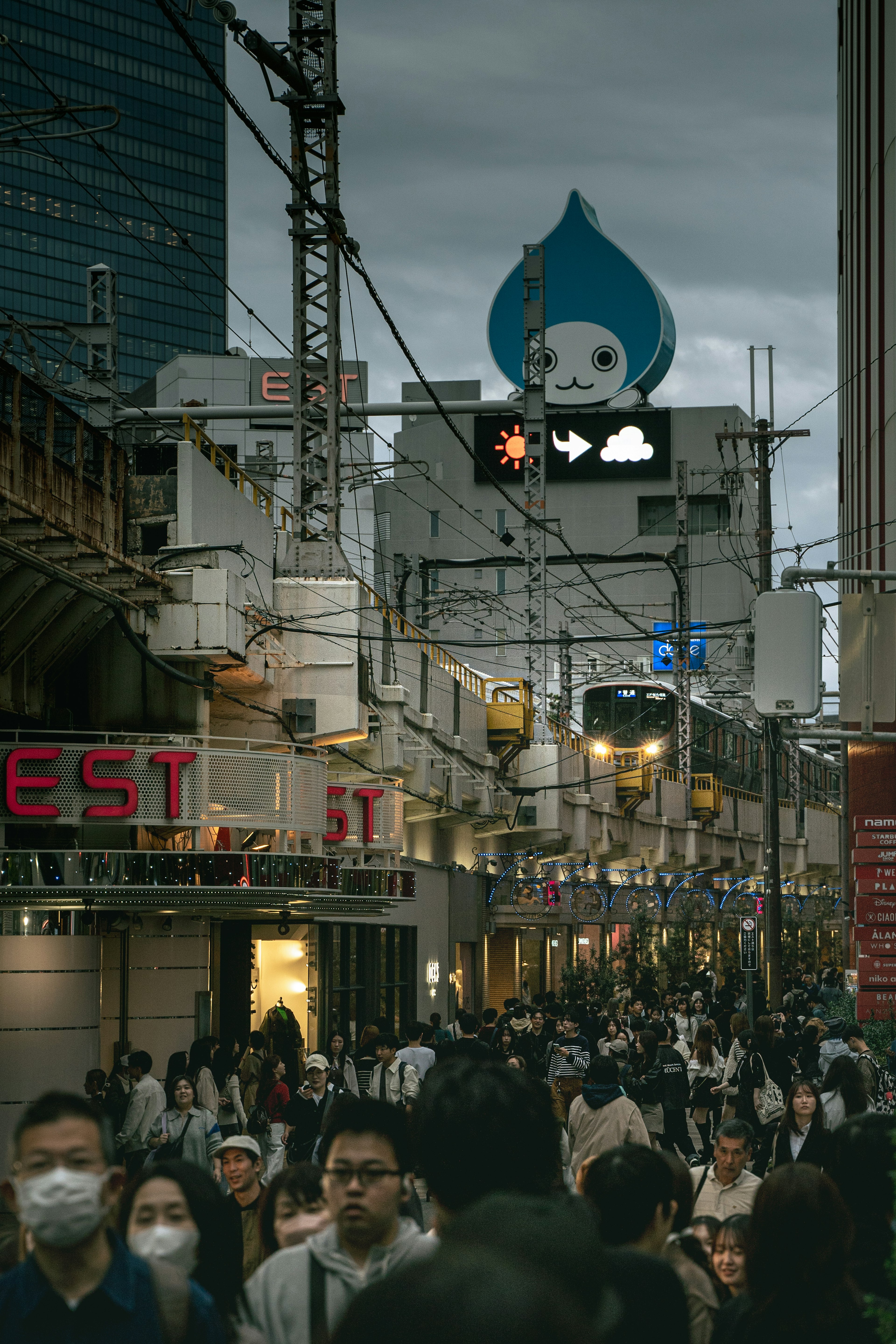 繁忙的城市街道場景，許多行人，背景中有藍色水滴形標誌