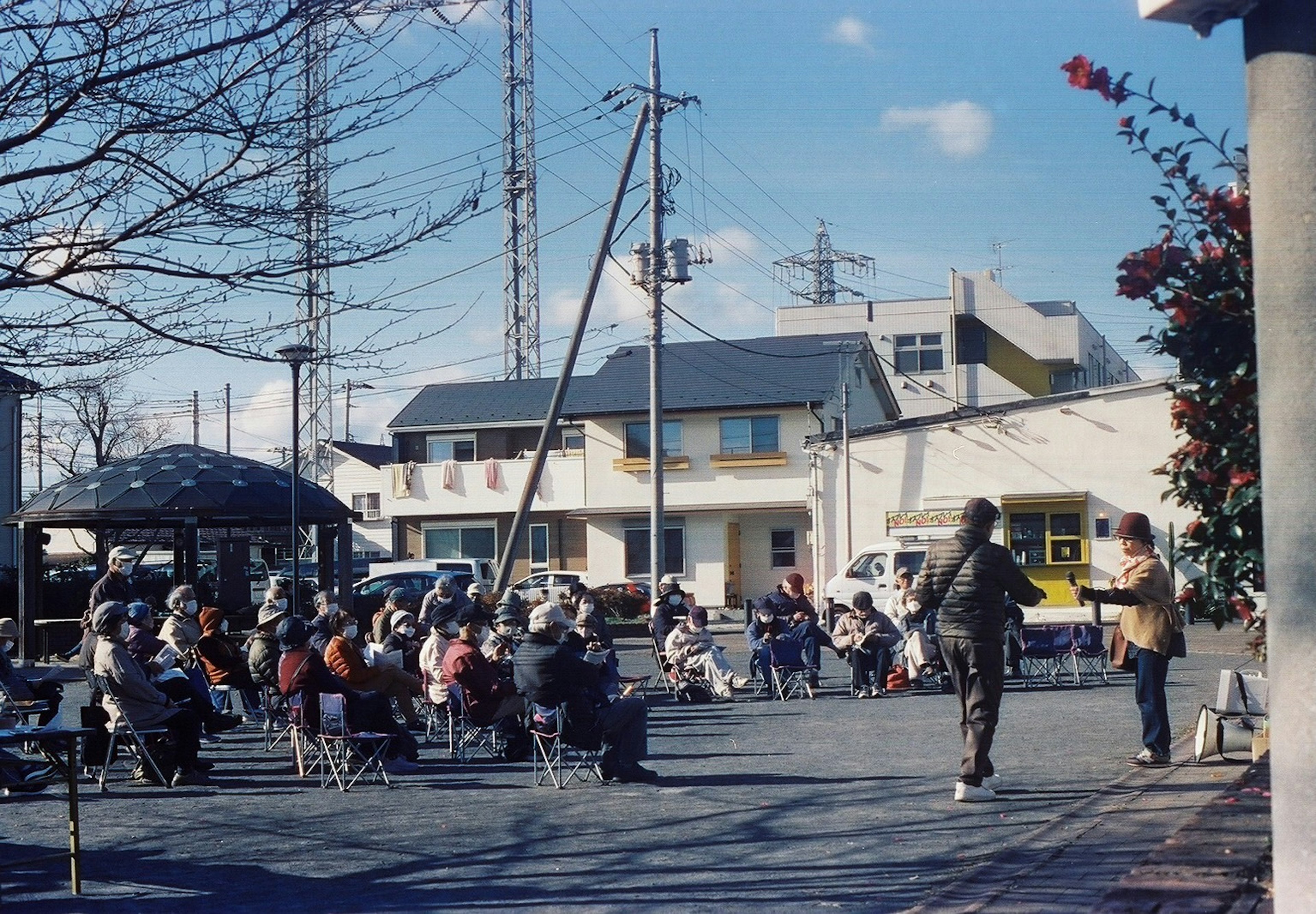 A group of people gathered in a park listening to a man speaking