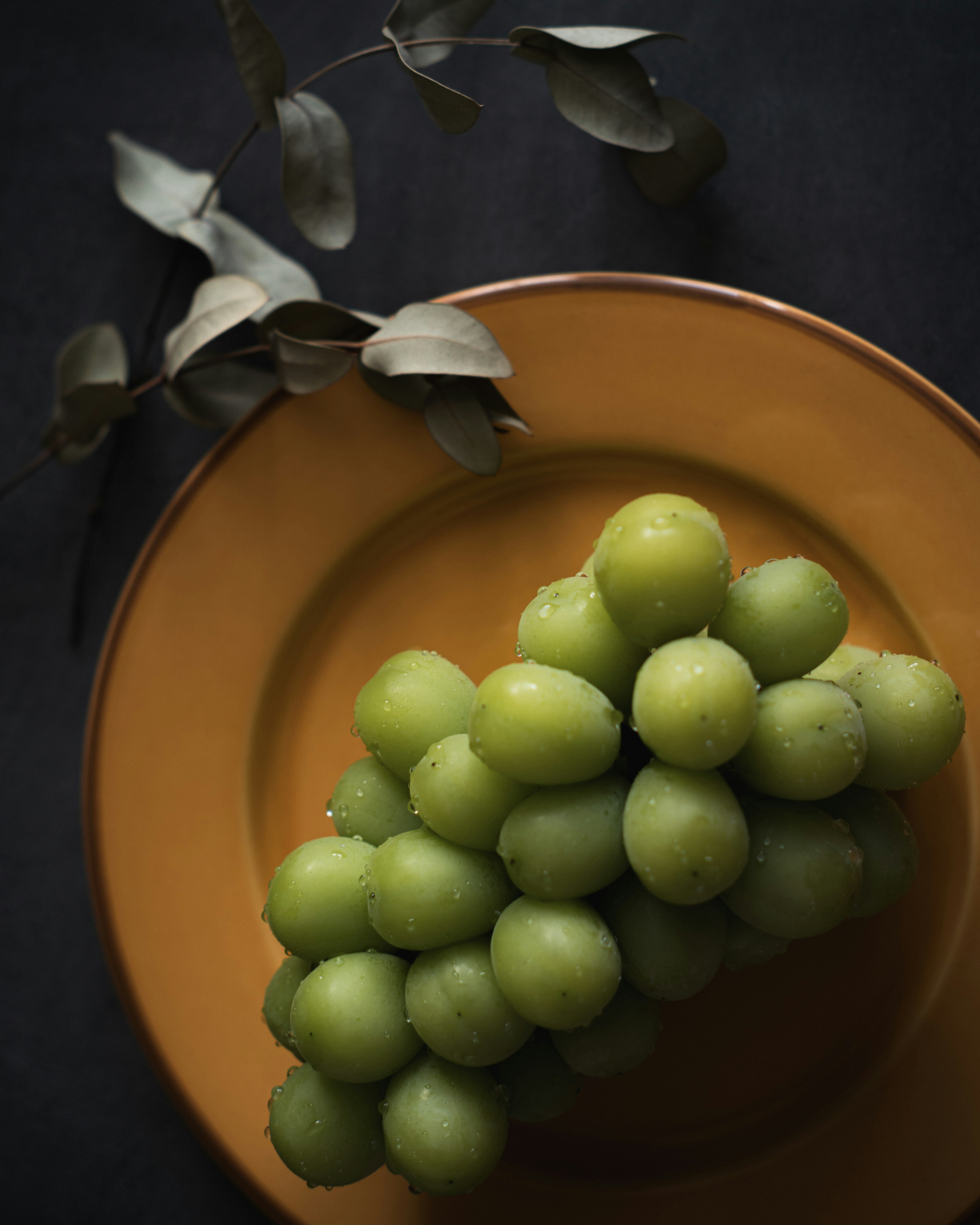 Un racimo de uvas verdes en un plato naranja con fondo oscuro