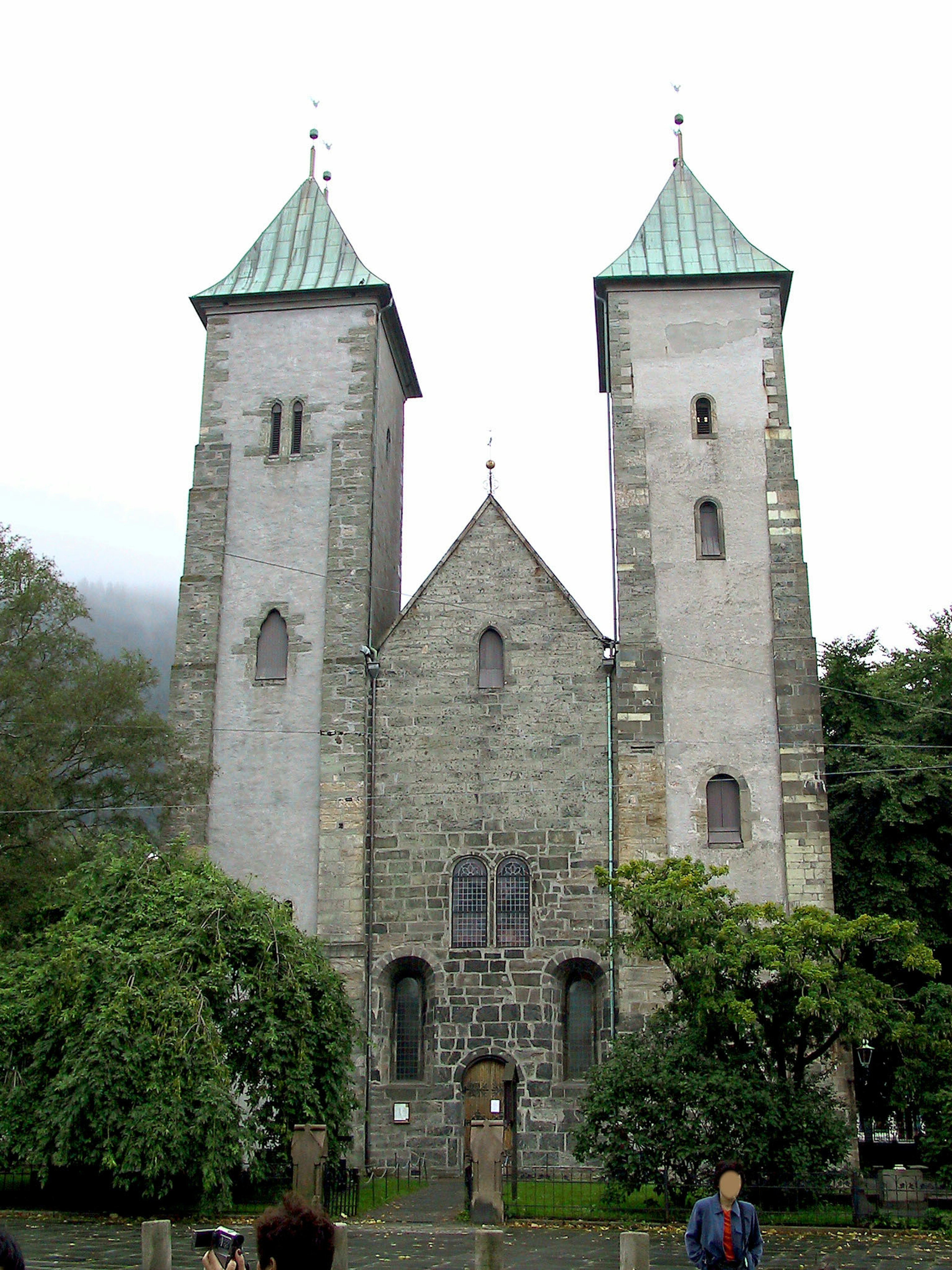 Stone church with two towers and green roofs surrounded by trees