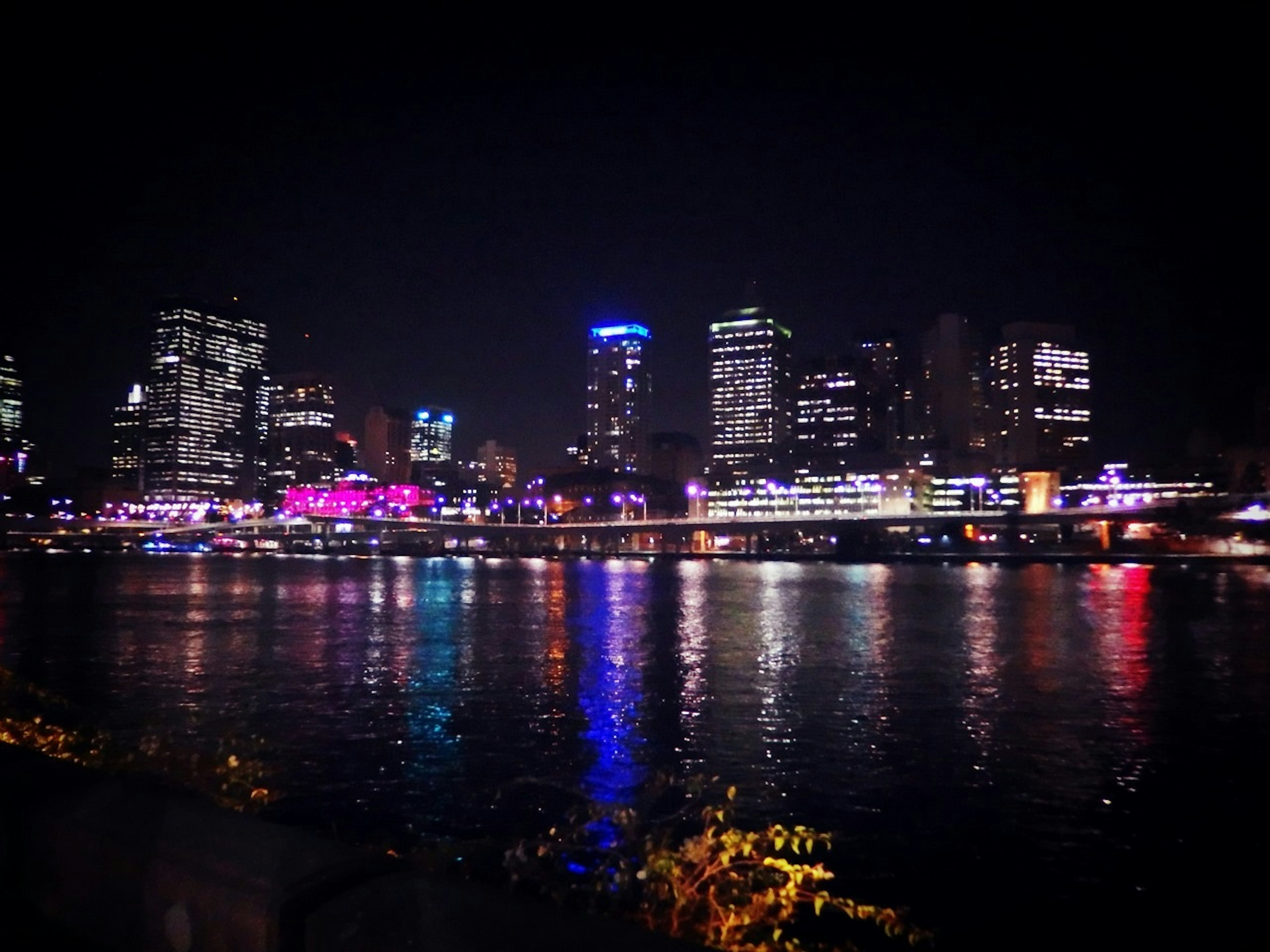 Vue nocturne d'une ligne d'horizon de ville avec des lumières colorées se reflétant sur la rivière