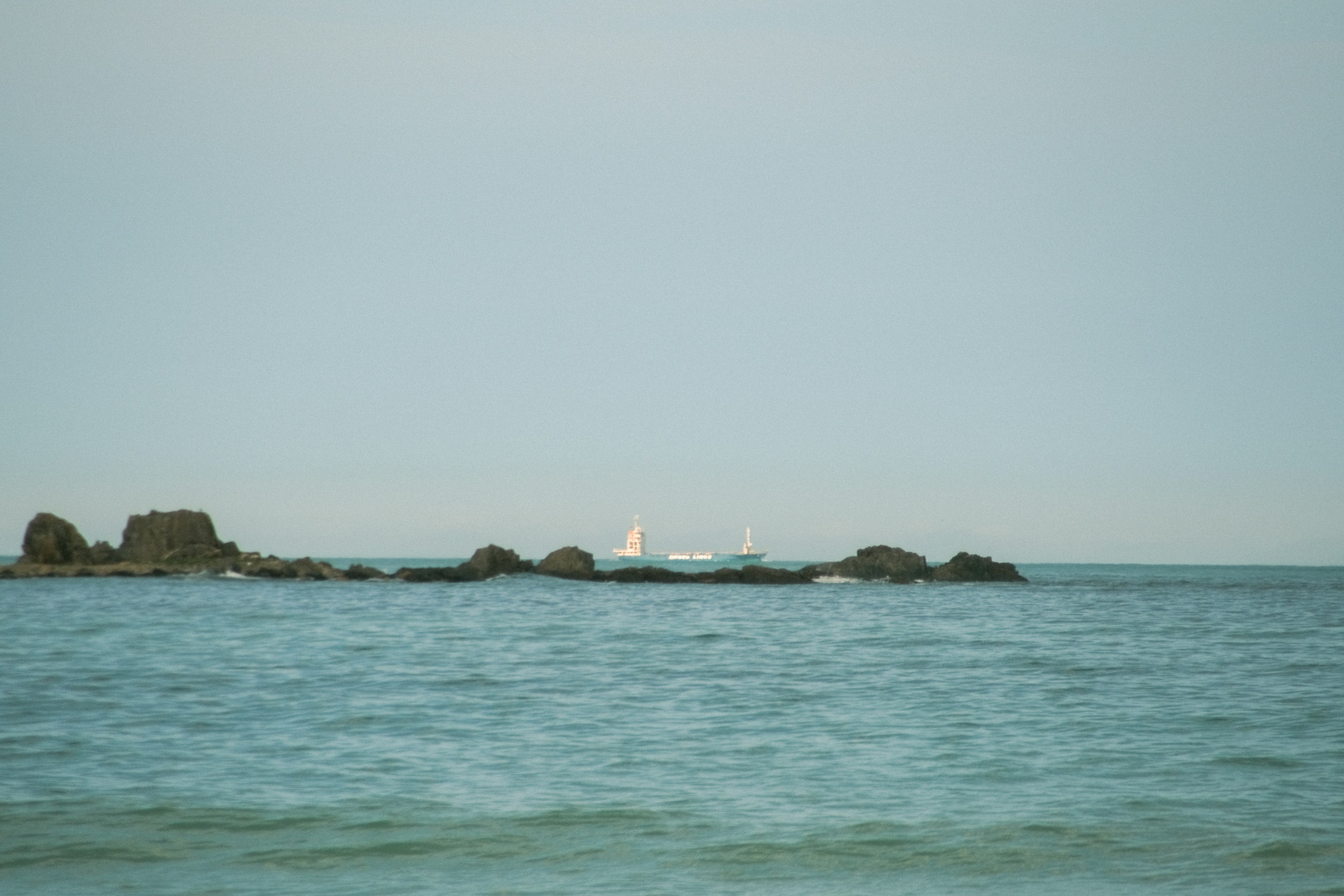 穏やかな海と遠くに見える帆船の風景