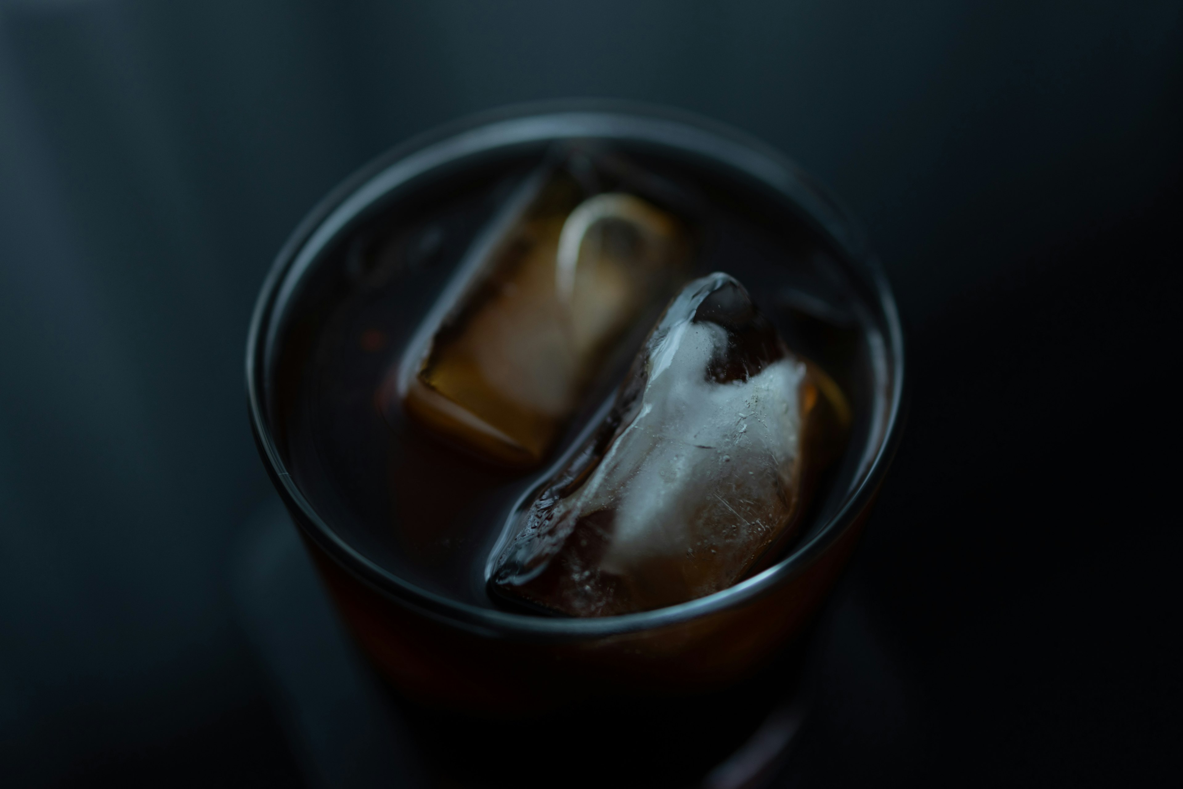 A glass with ice cubes containing a dark beverage