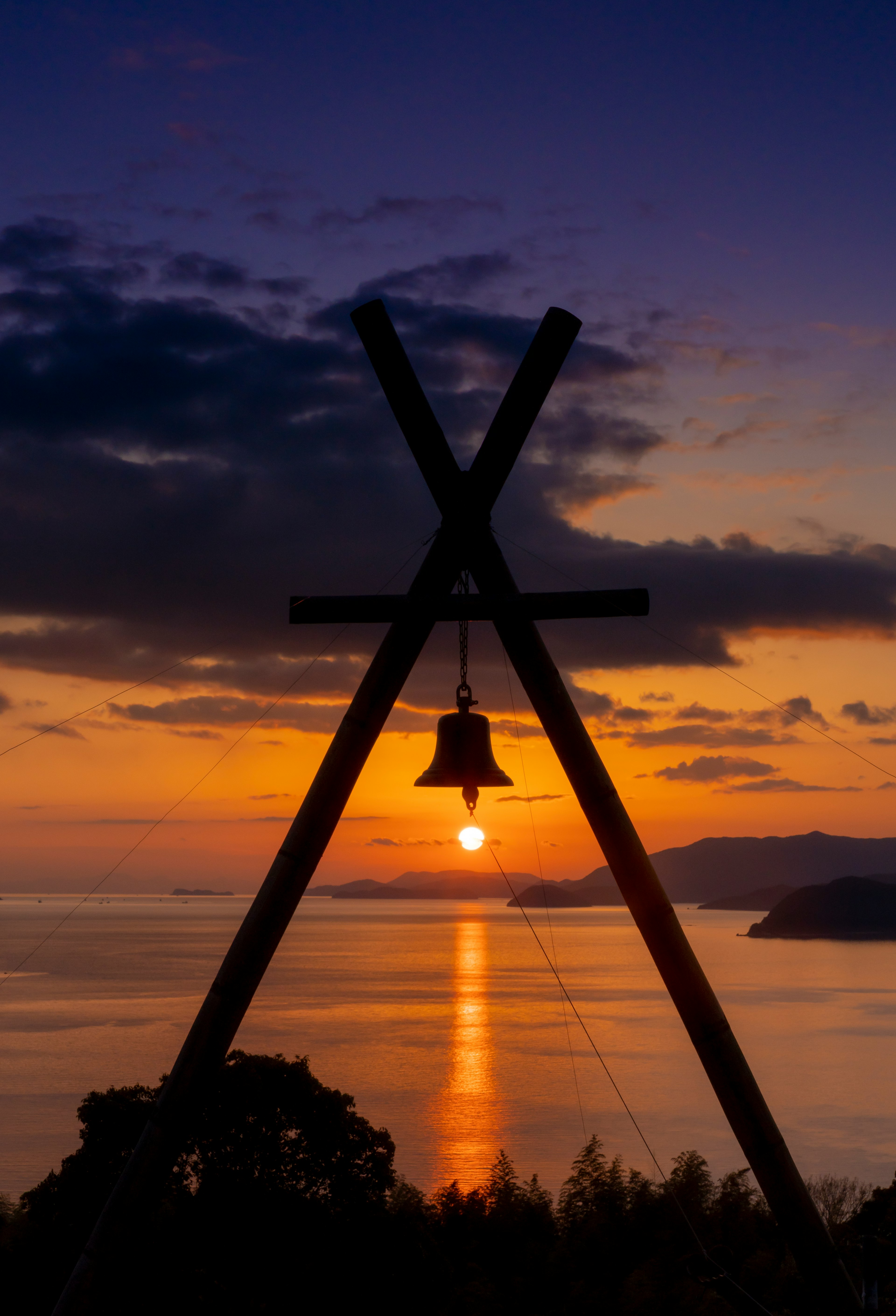 夕日を背景にした鐘のシルエットと海