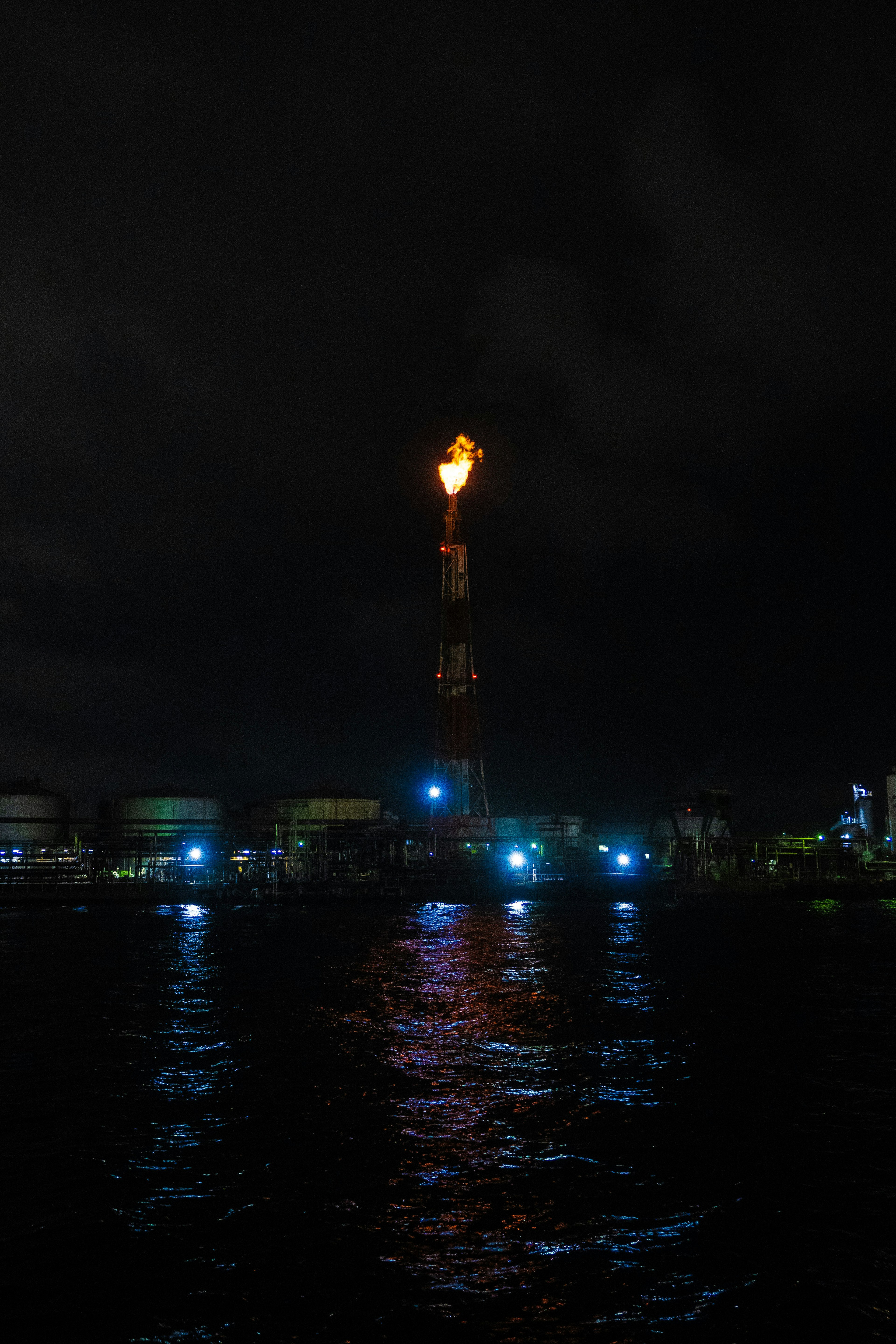 Industrial smokestack with flame reflected in dark water