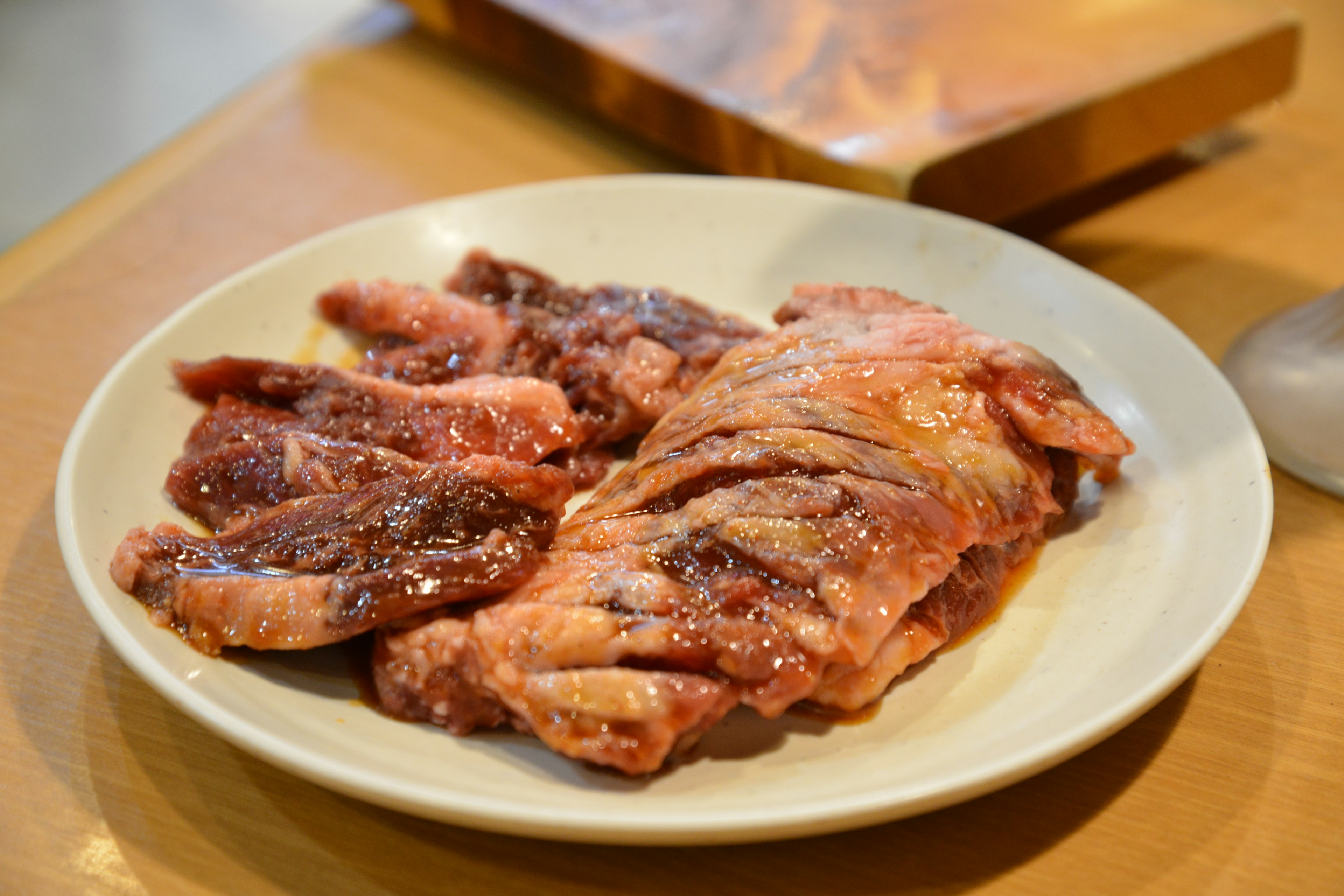 Ein Teller mit mariniertem Fleisch zum Grillen in lebhaften Rot- und Brauntönen ein Holzschneidebrett im Hintergrund