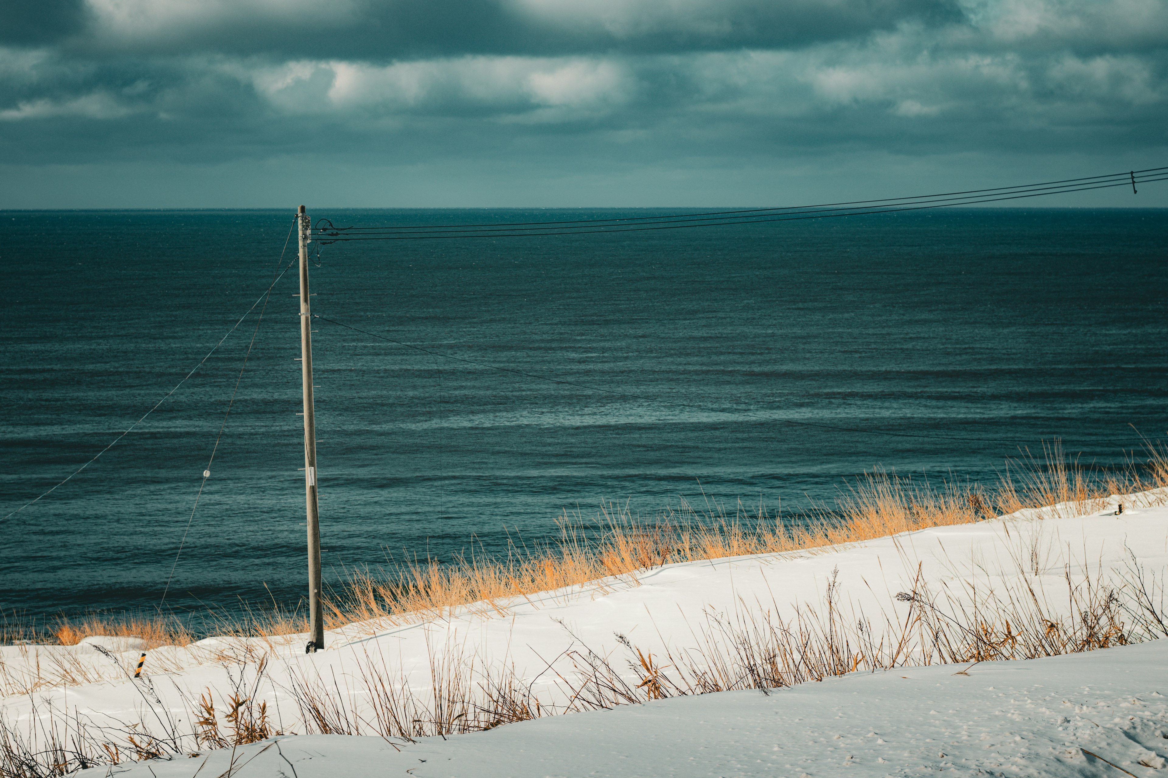 A power pole on a snowy hillside overlooking a calm sea