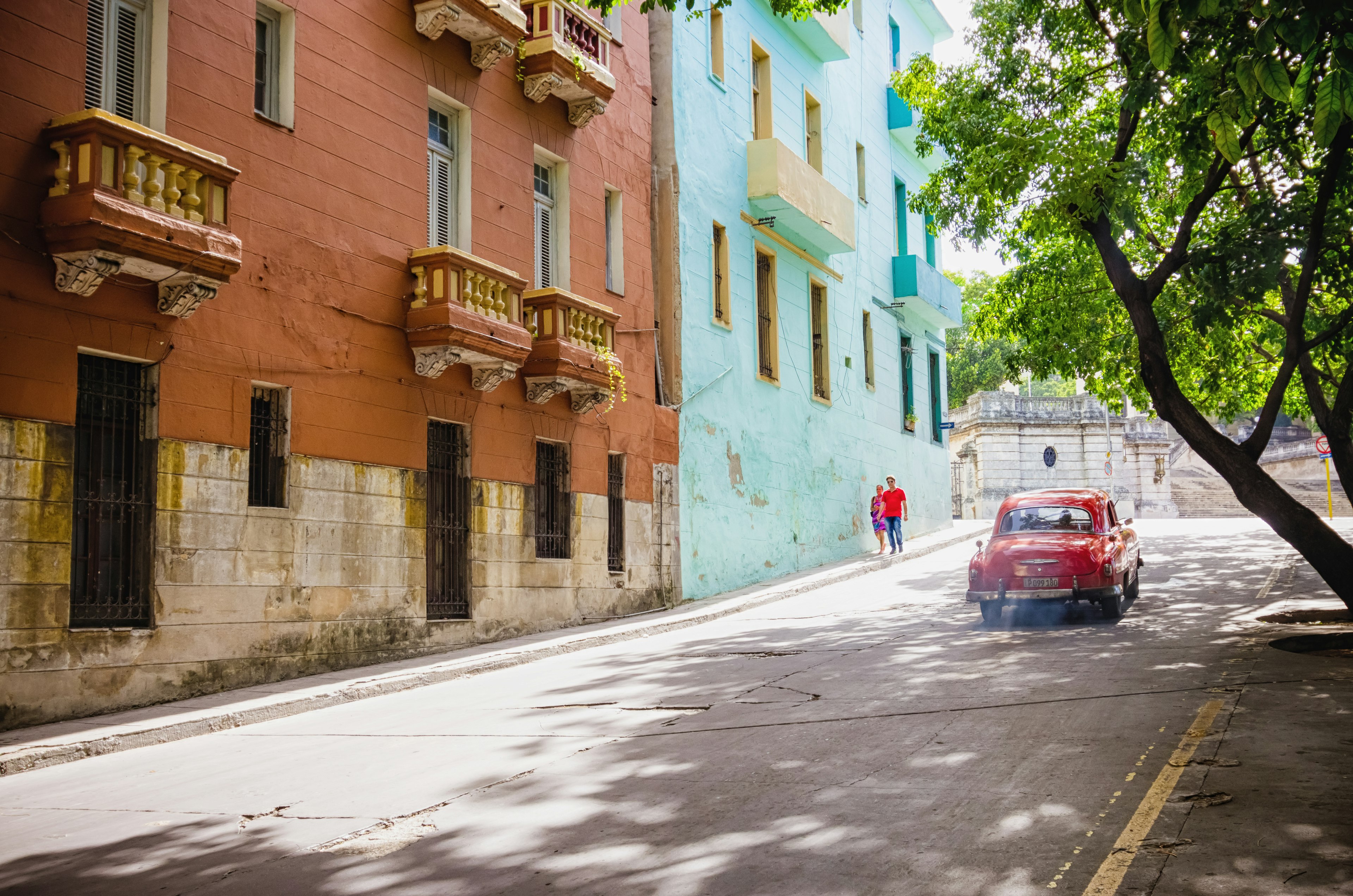 A colorful street scene with a red car driving past vibrant buildings