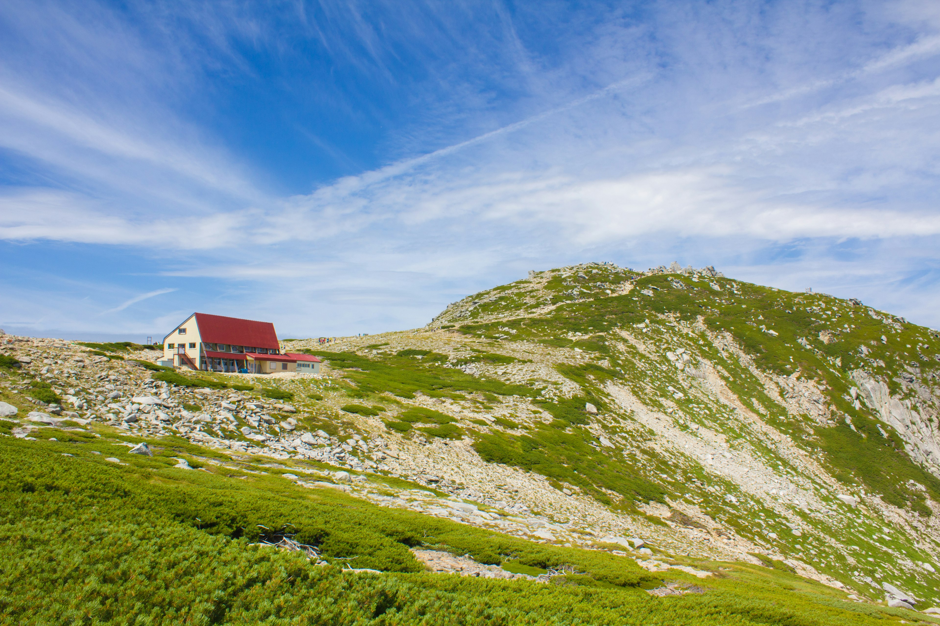 Una baita con tetto rosso su una collina verde sotto un cielo blu con nuvole bianche