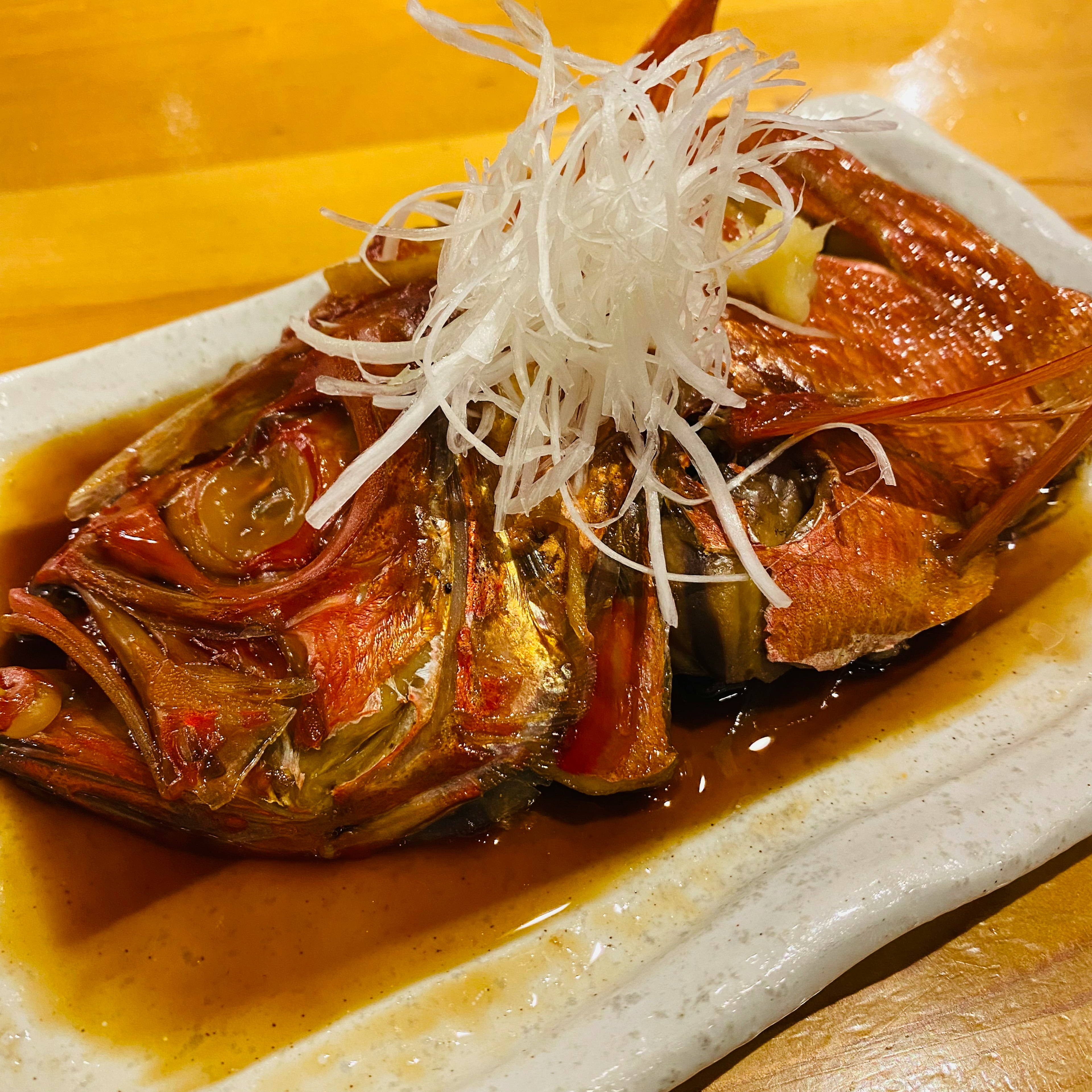 白い皿に盛り付けられた煮魚に細切りのネギがトッピングされた料理