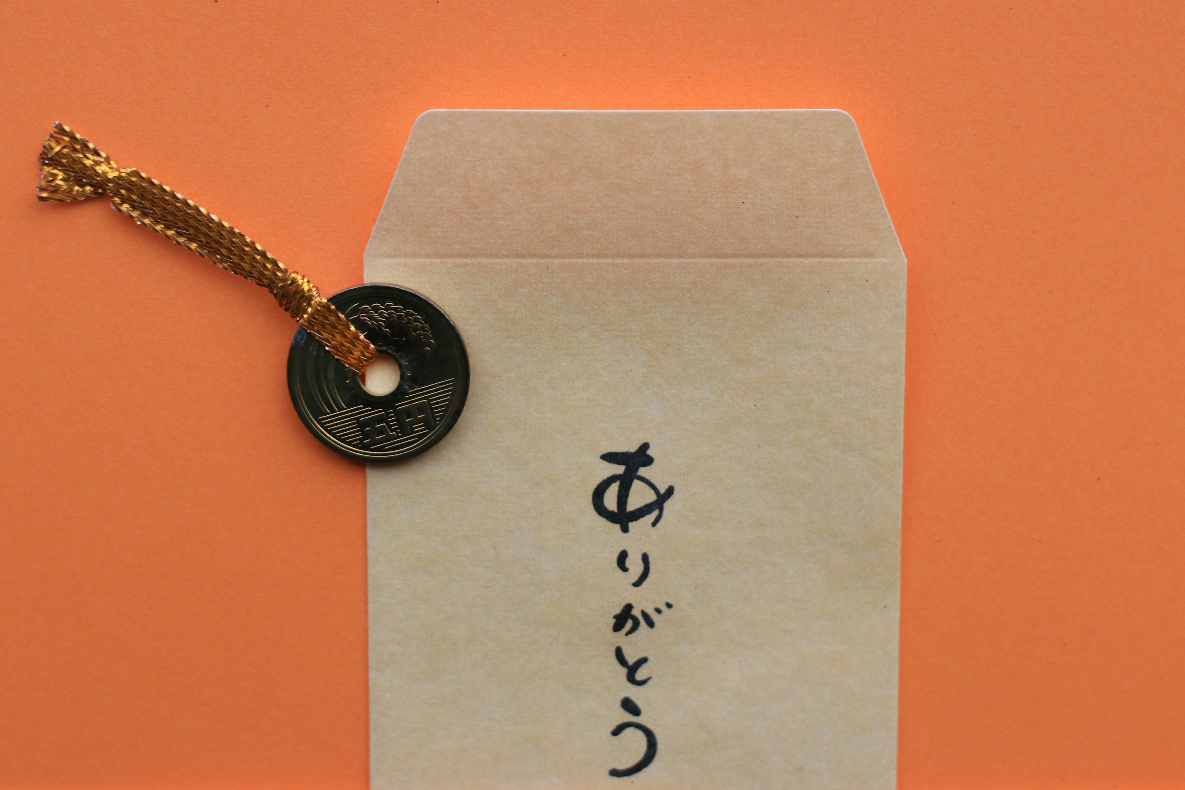 A Japanese thank you card with a black coin attached by a golden string on an orange background