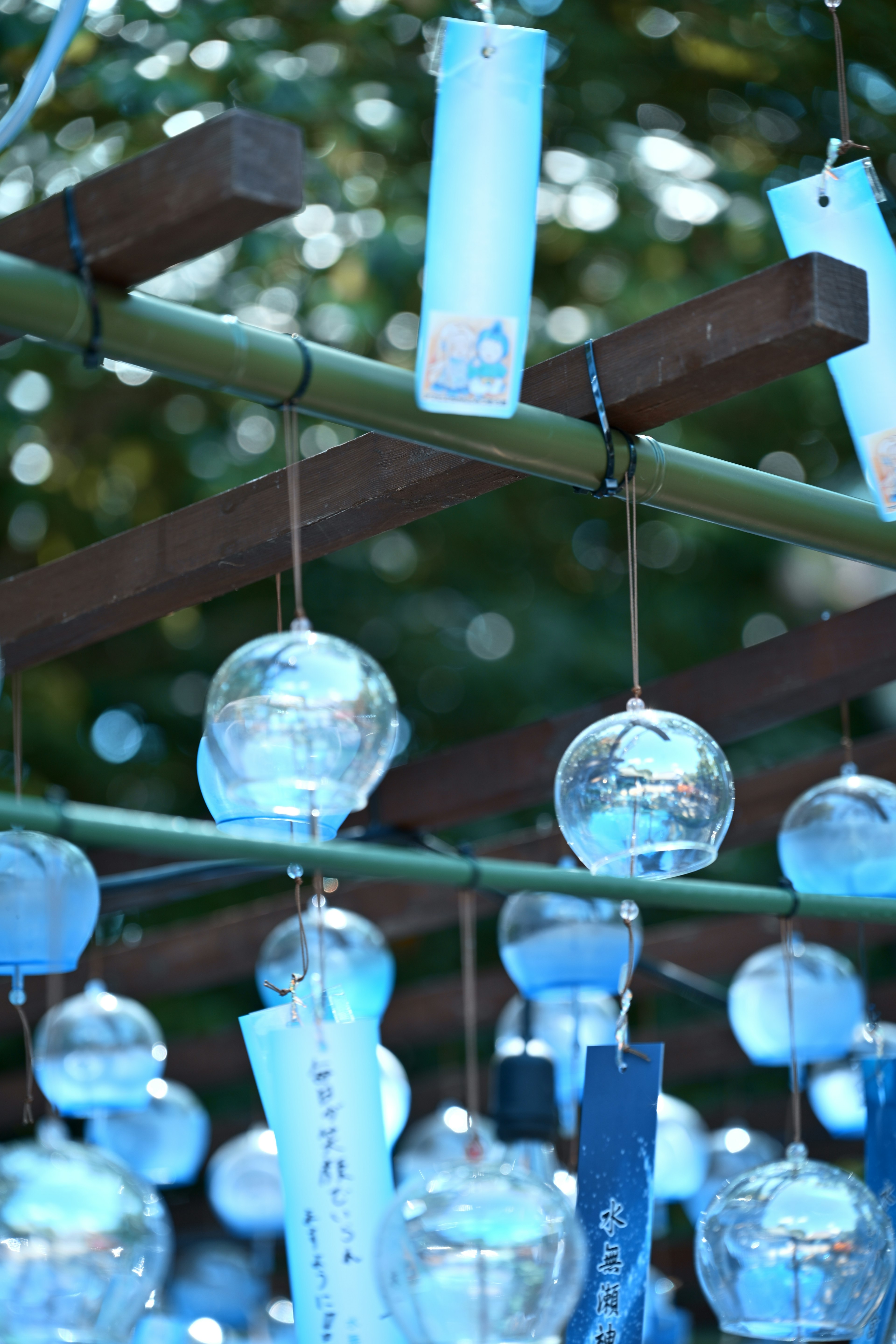 Blue wind chimes hanging from a bamboo structure with a blurred background