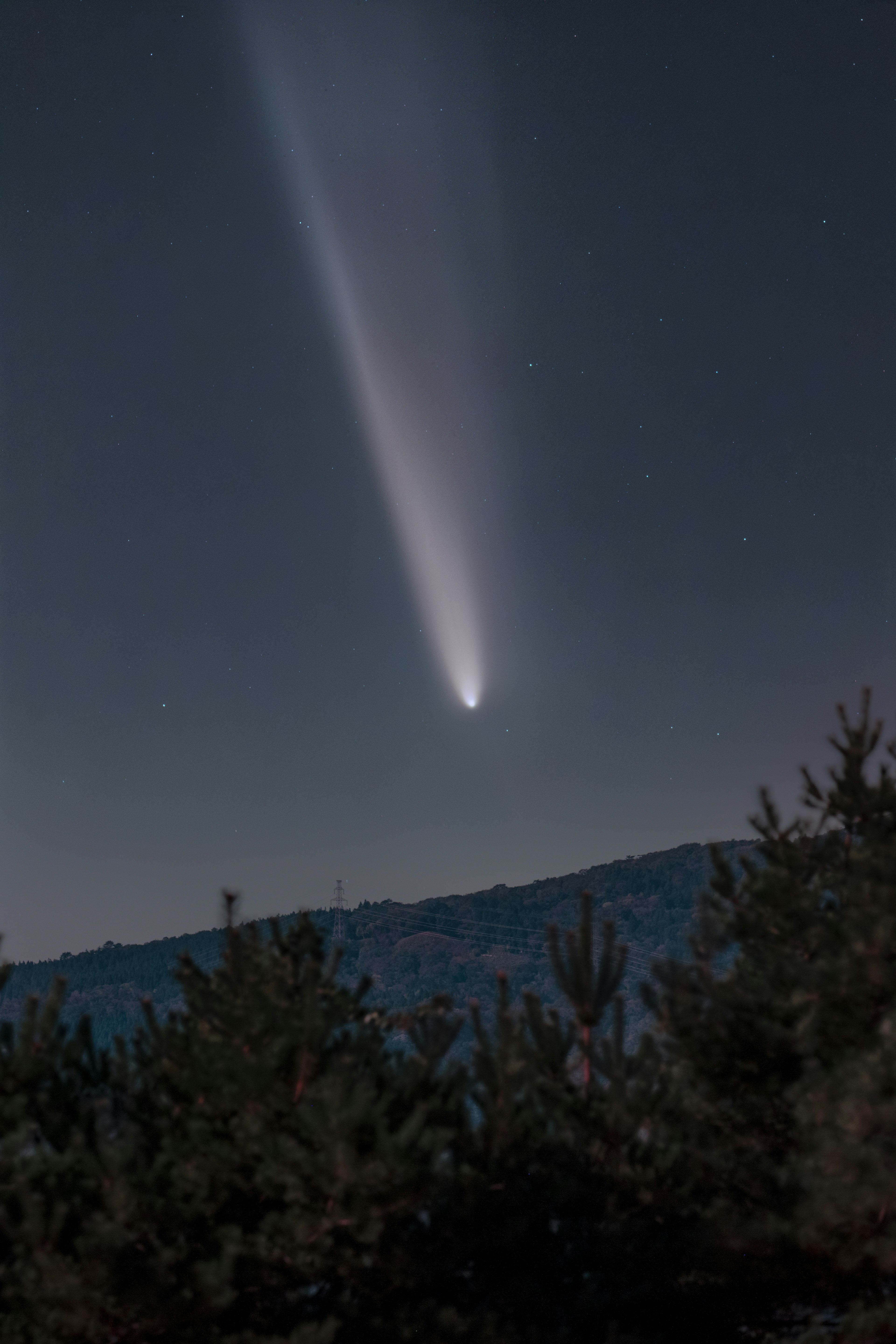 夜空に輝く彗星と山のシルエット