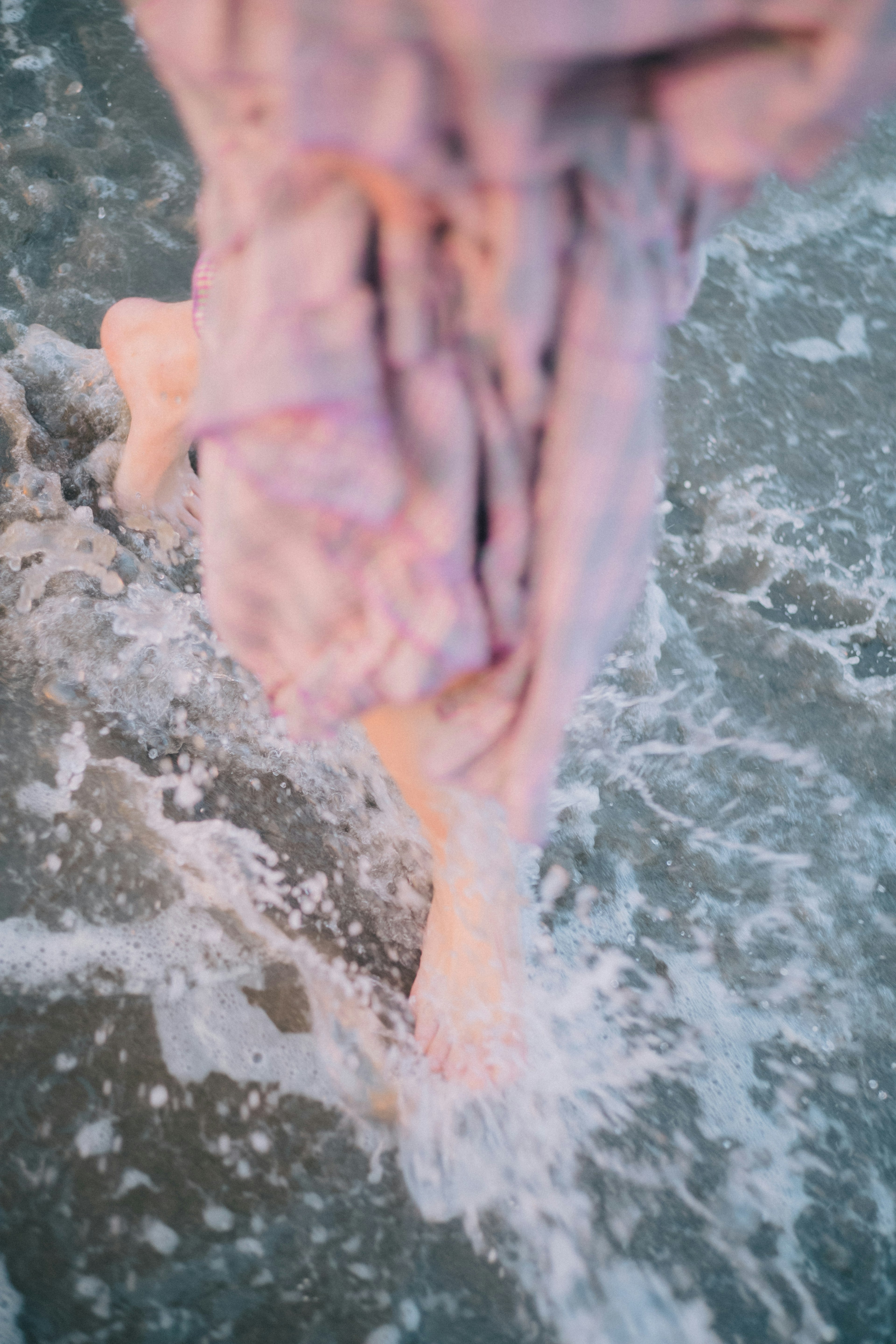 Primo piano di piedi che camminano nell'acqua bassa sulla spiaggia indossando un vestito rosa