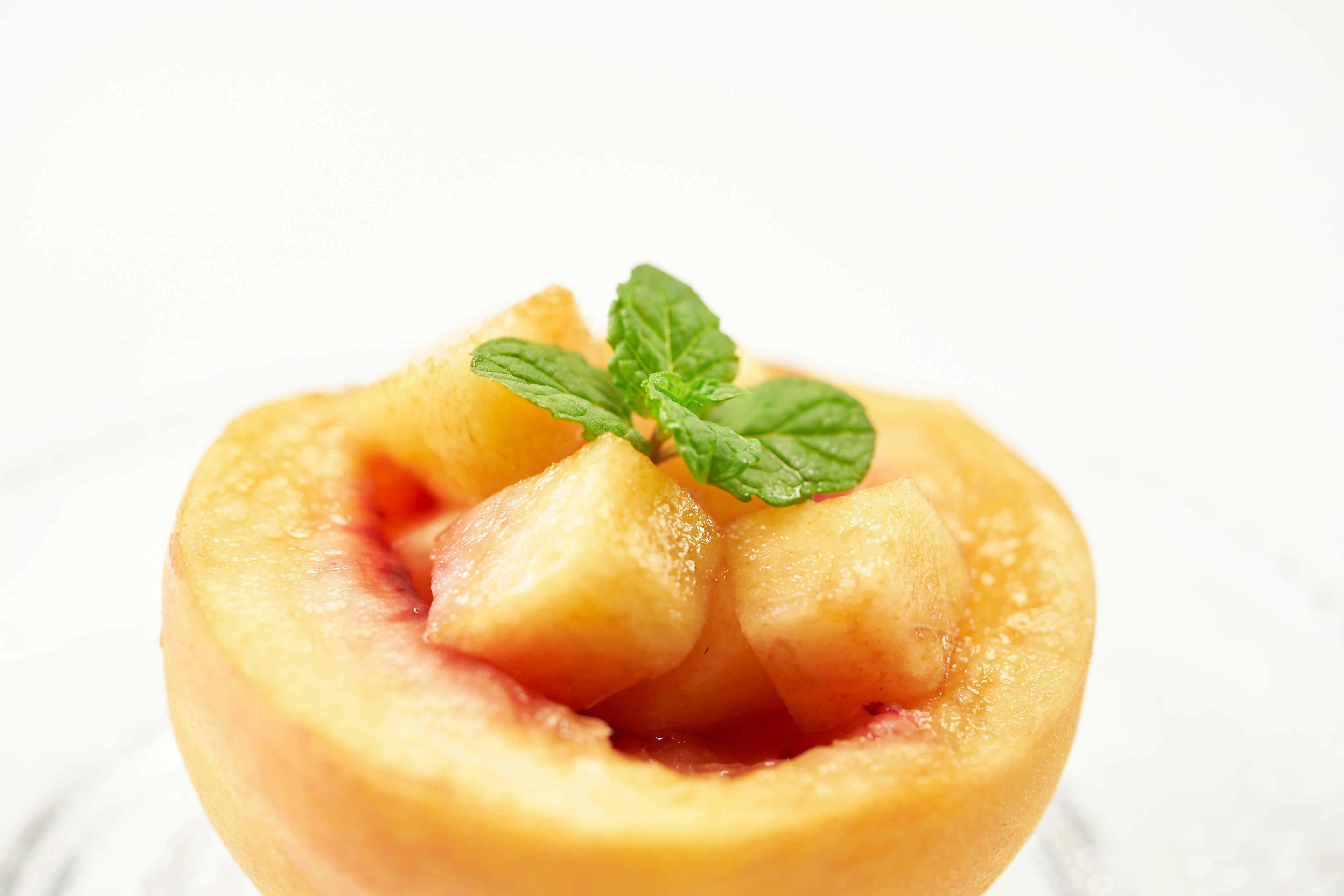 Mitad de durazno con trozos de fruta y una hoja de menta encima