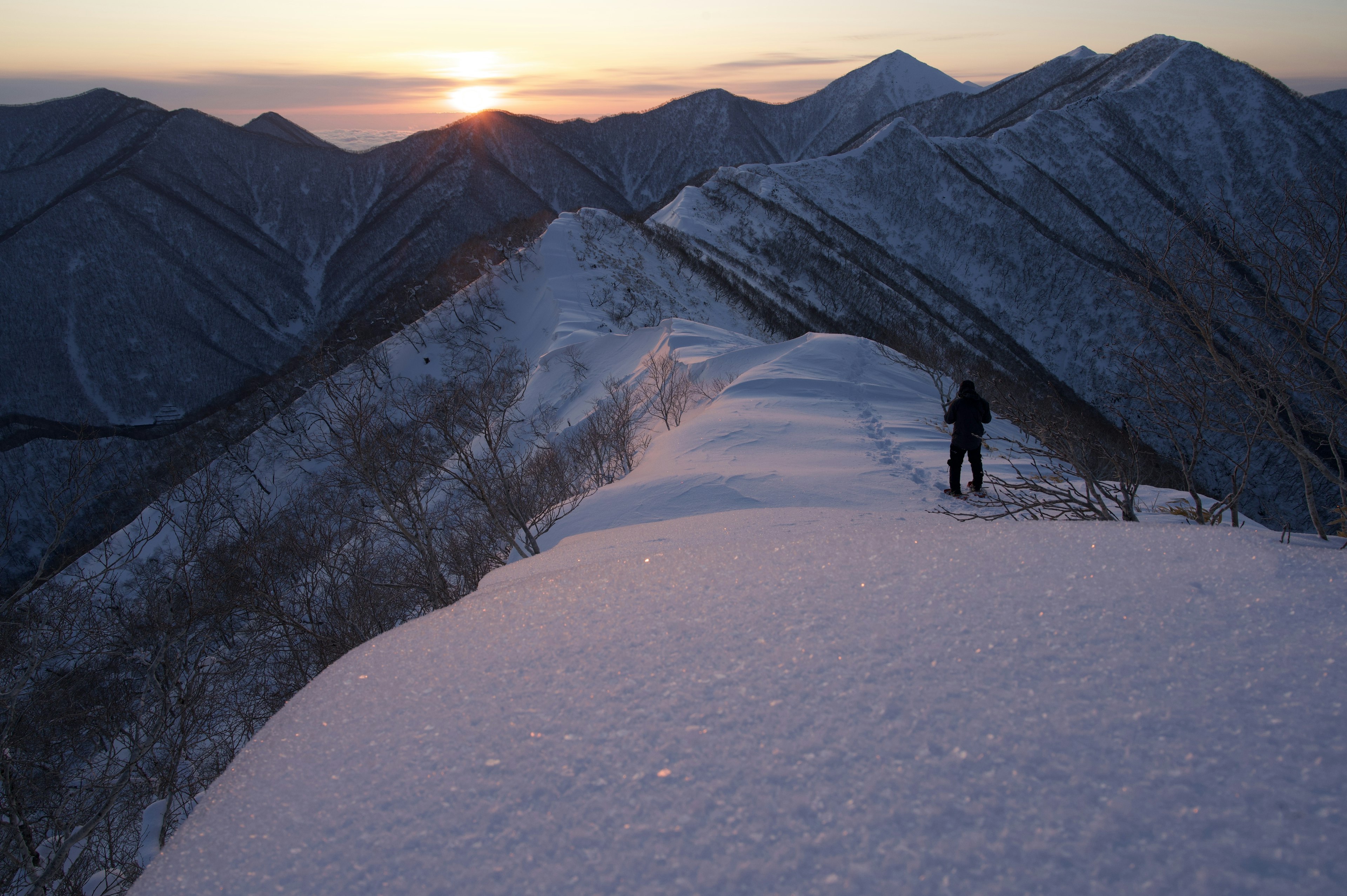 Silueta de un excursionista en una cresta montañosa nevada con un amanecer al fondo