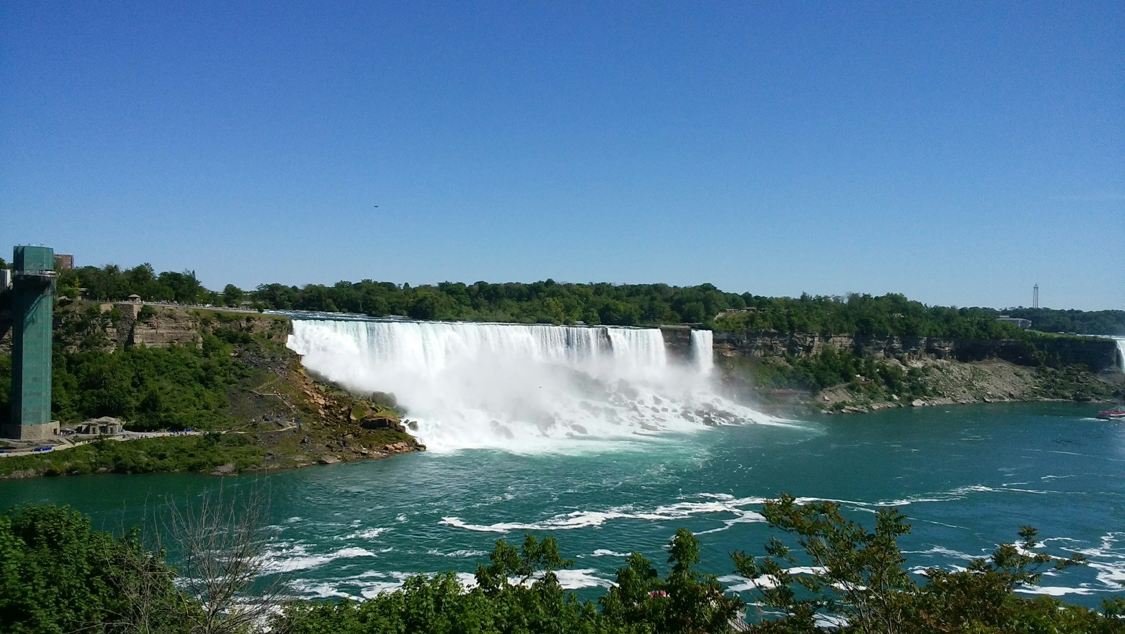 Pemandangan megah Air Terjun Niagara dikelilingi pepohonan hijau di bawah langit biru