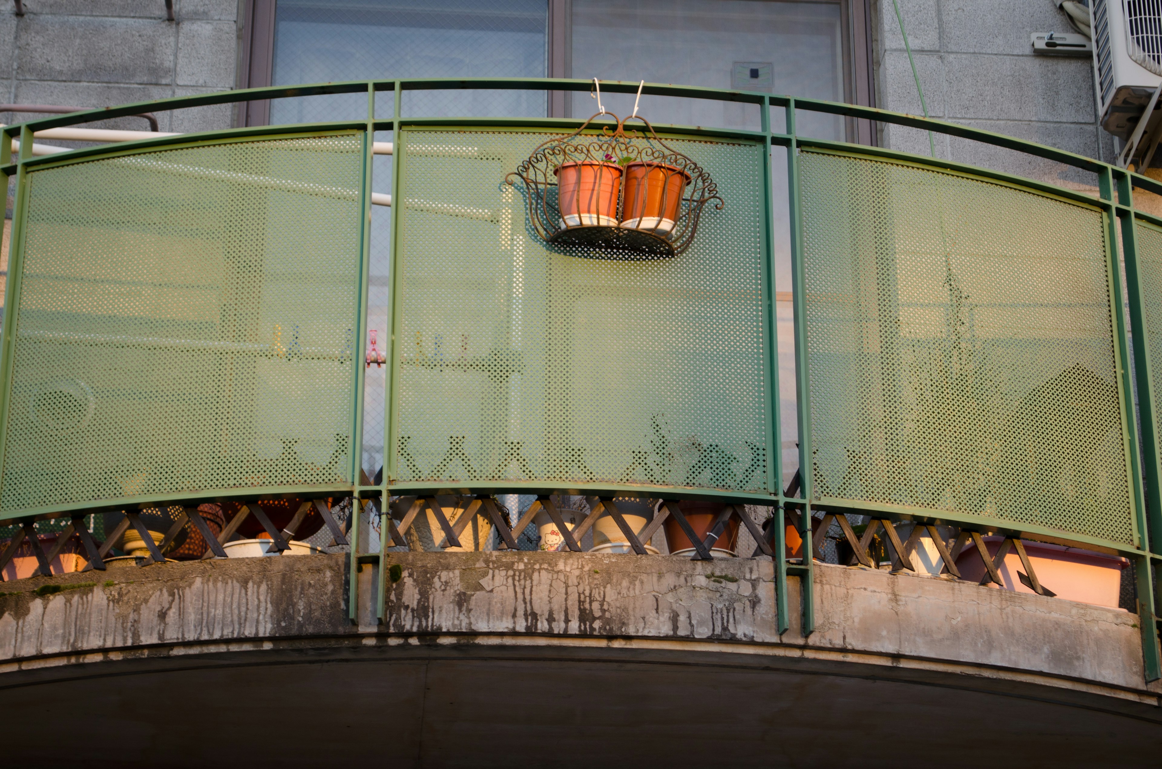 Orange basket hanging on a green glass balcony with visible plants