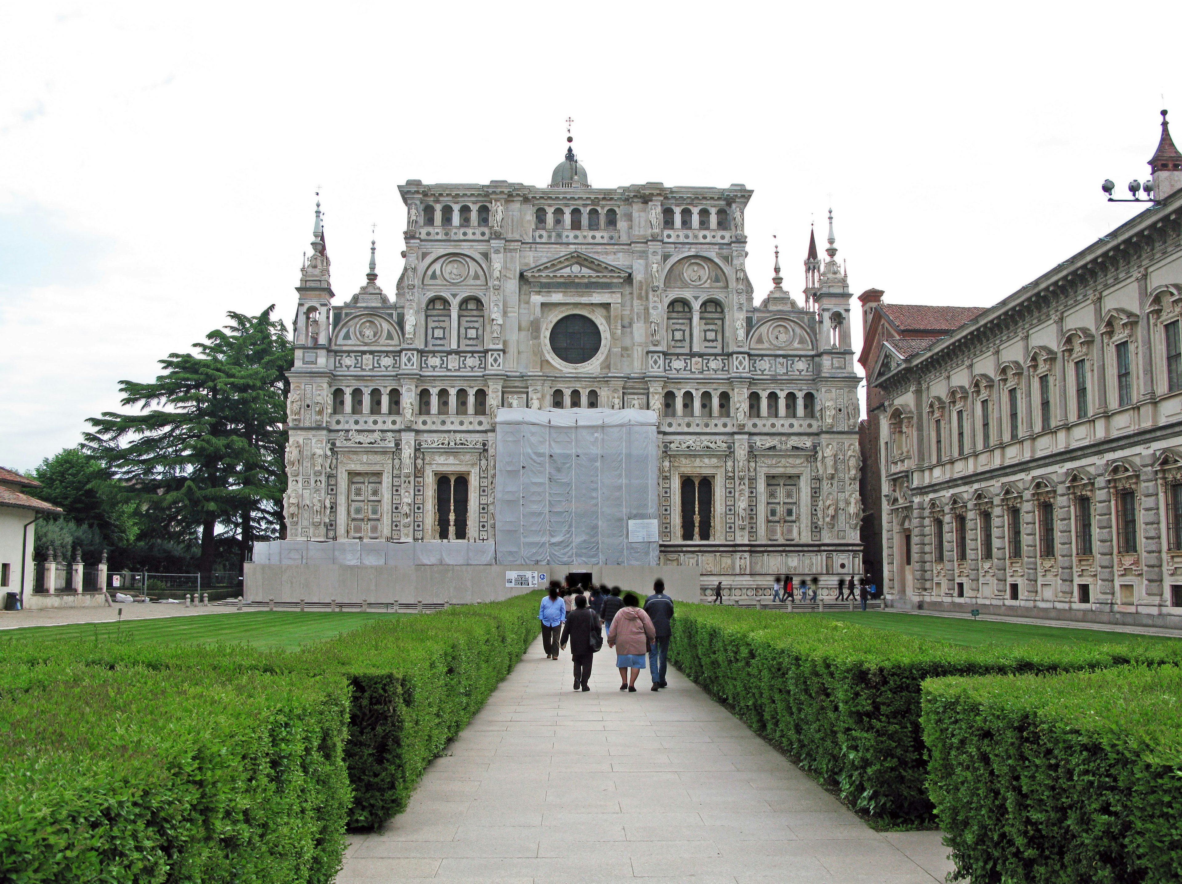 People walking along a pathway in a garden with a beautiful architectural facade in the background