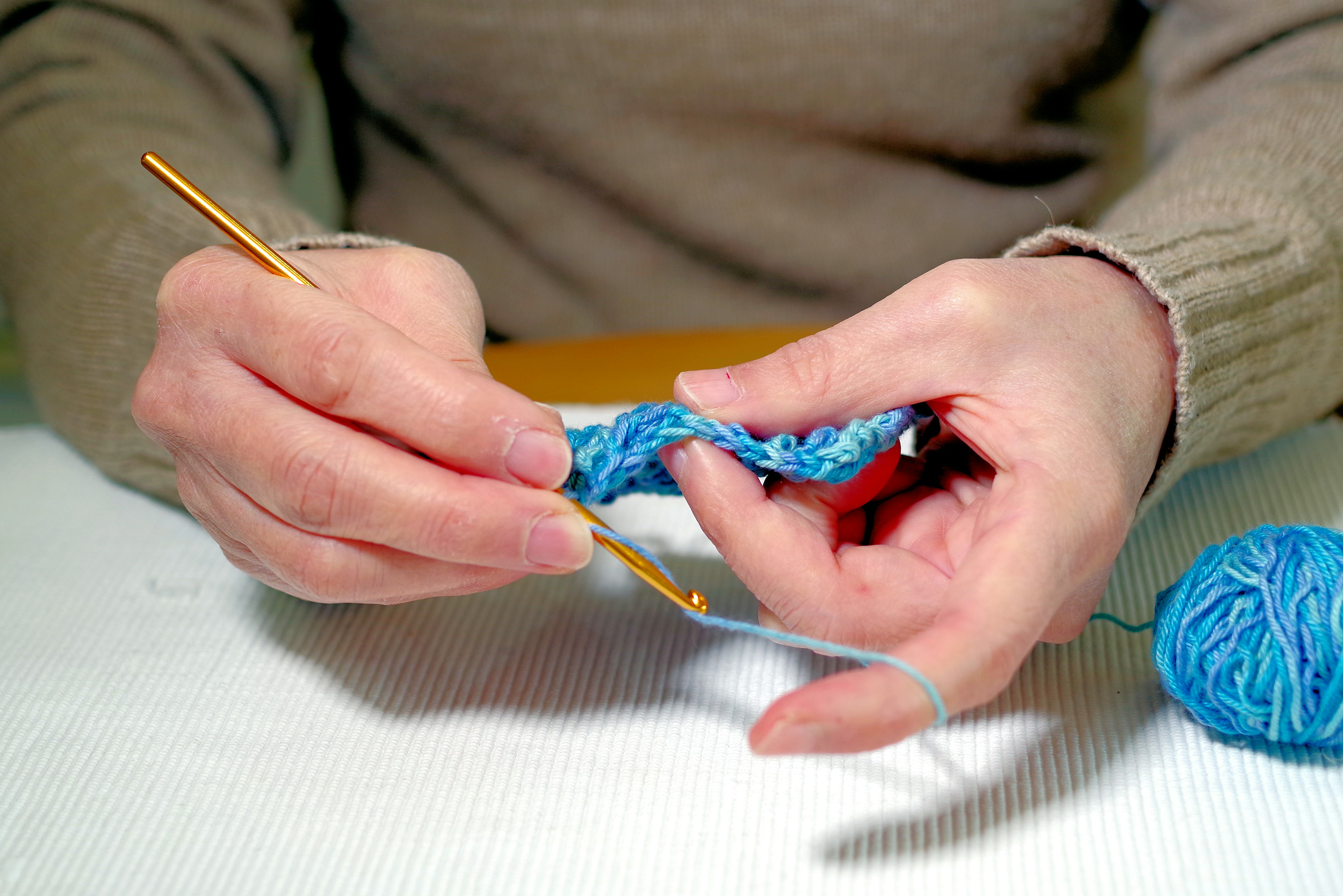 Primo piano di mani che lavorano a uncinetto con filato blu