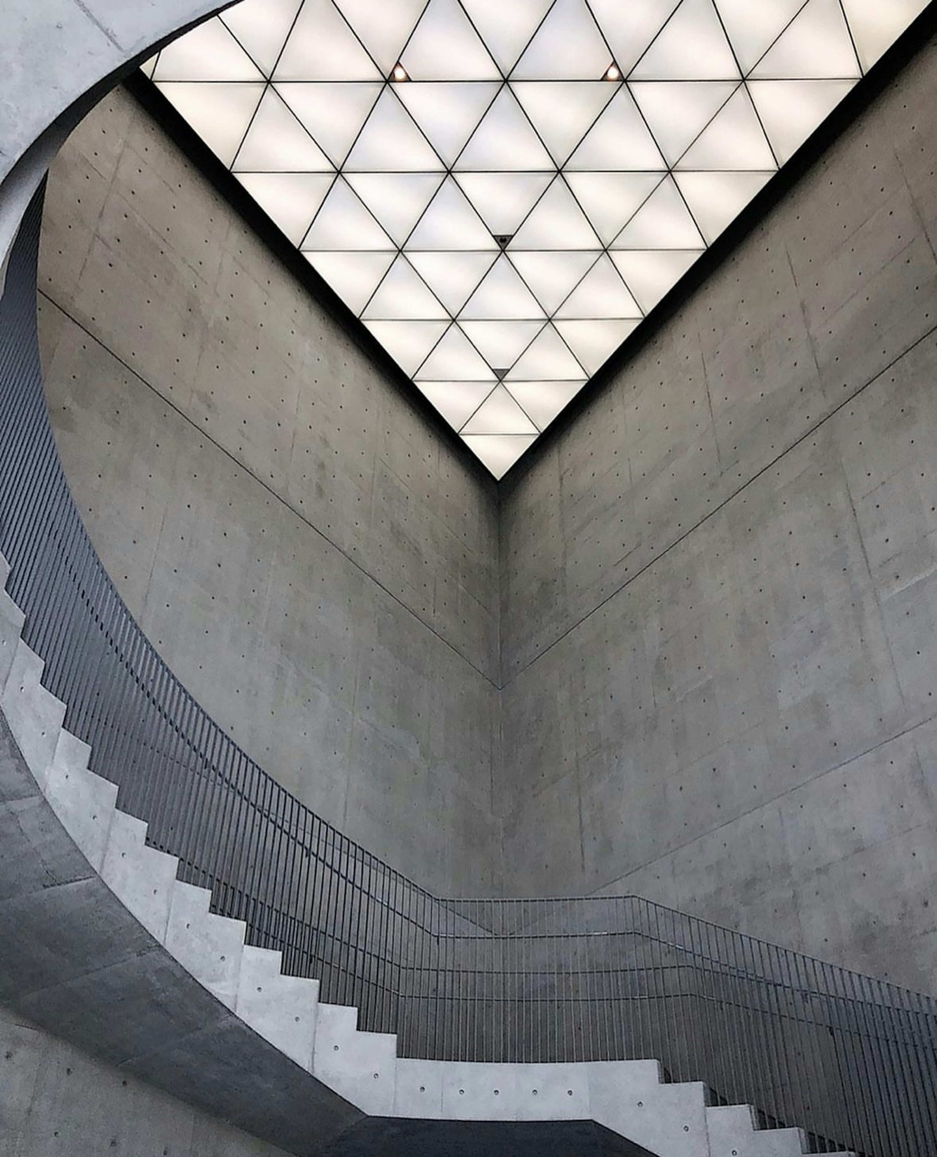 Interior of a spiral staircase with concrete walls and a triangular ceiling