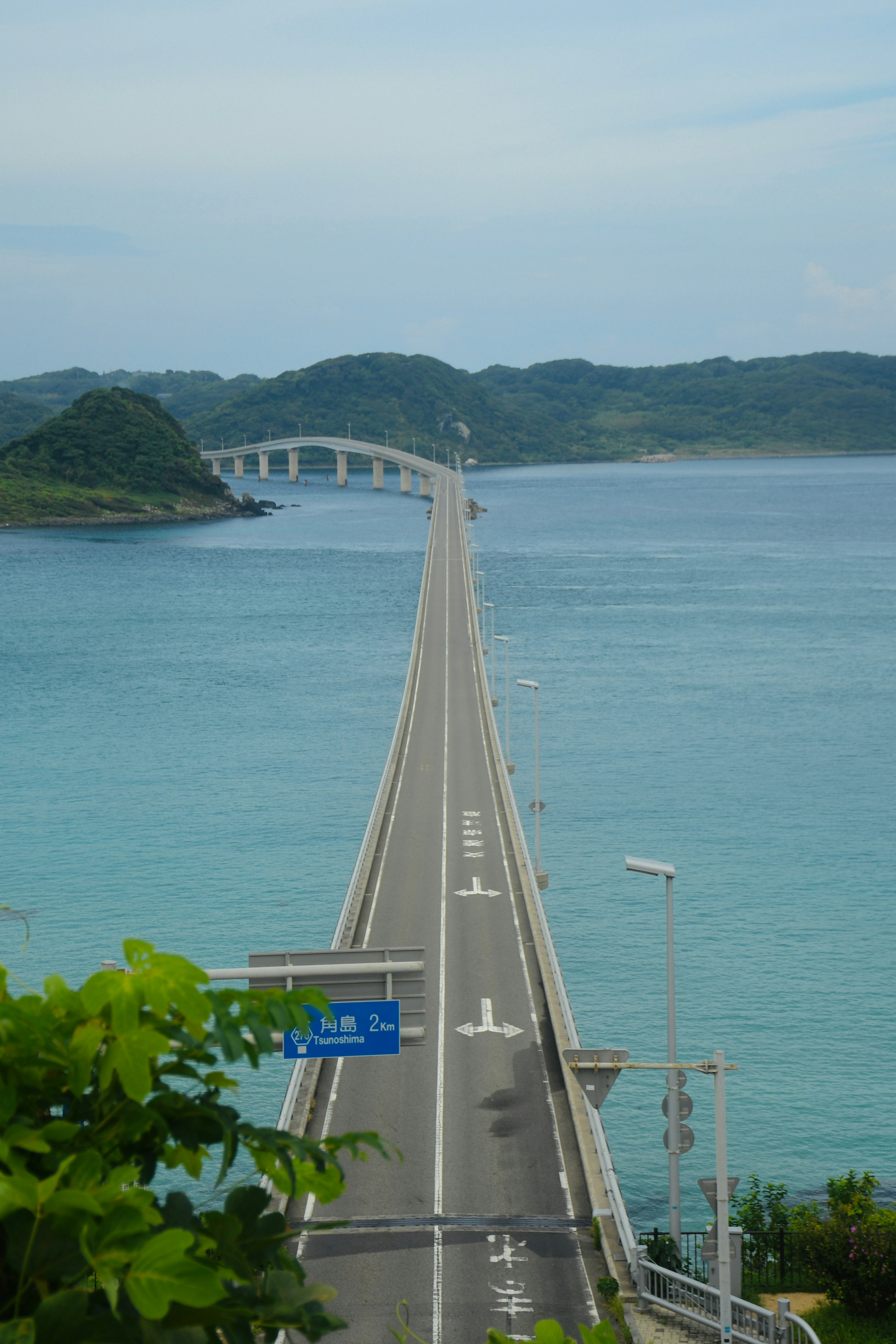 Langer Brücke über das blaue Meer mit grünen Hügeln im Hintergrund