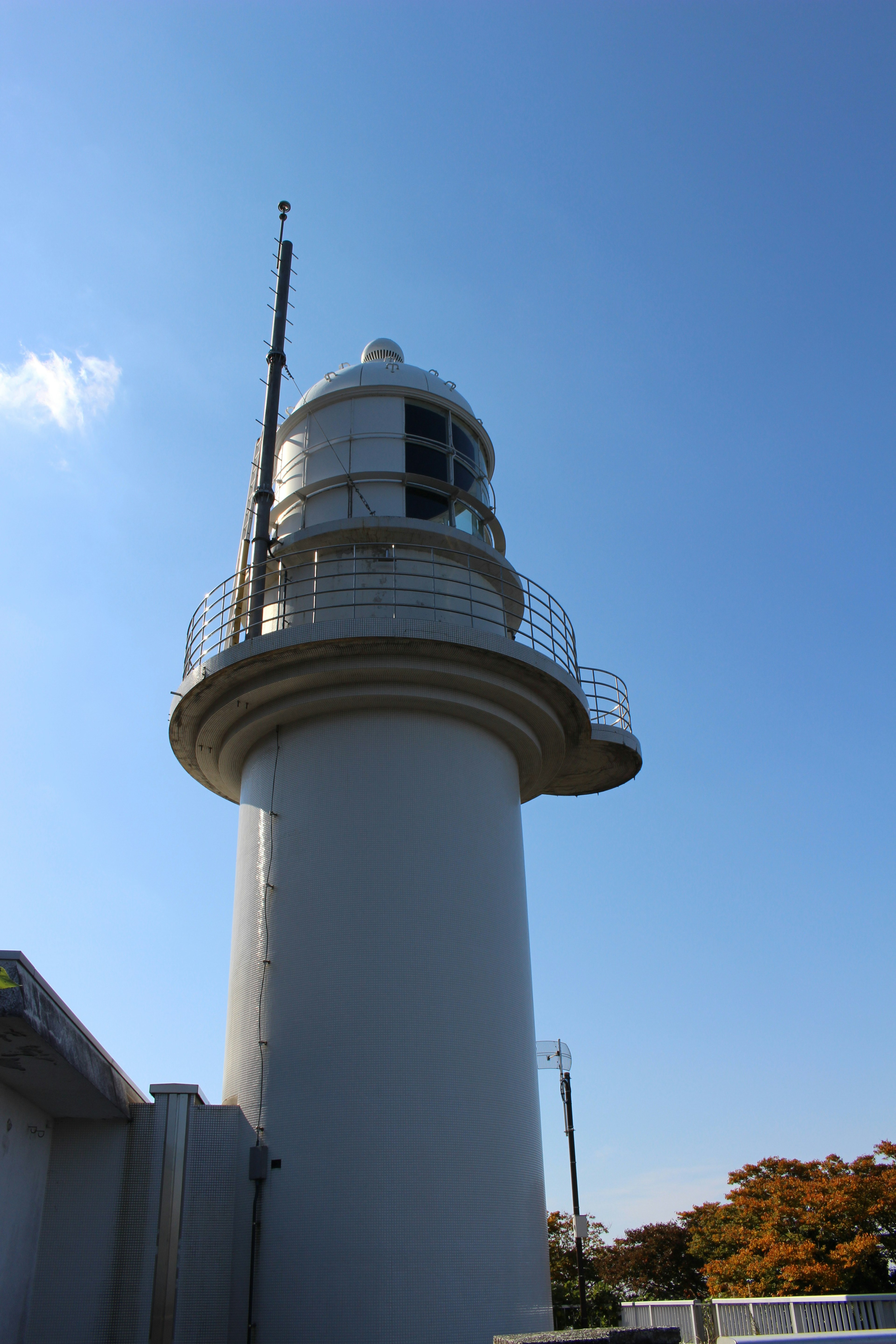 Foto di un faro sotto un cielo blu Il faro è una struttura cilindrica bianca con una lente e un'antenna in cima