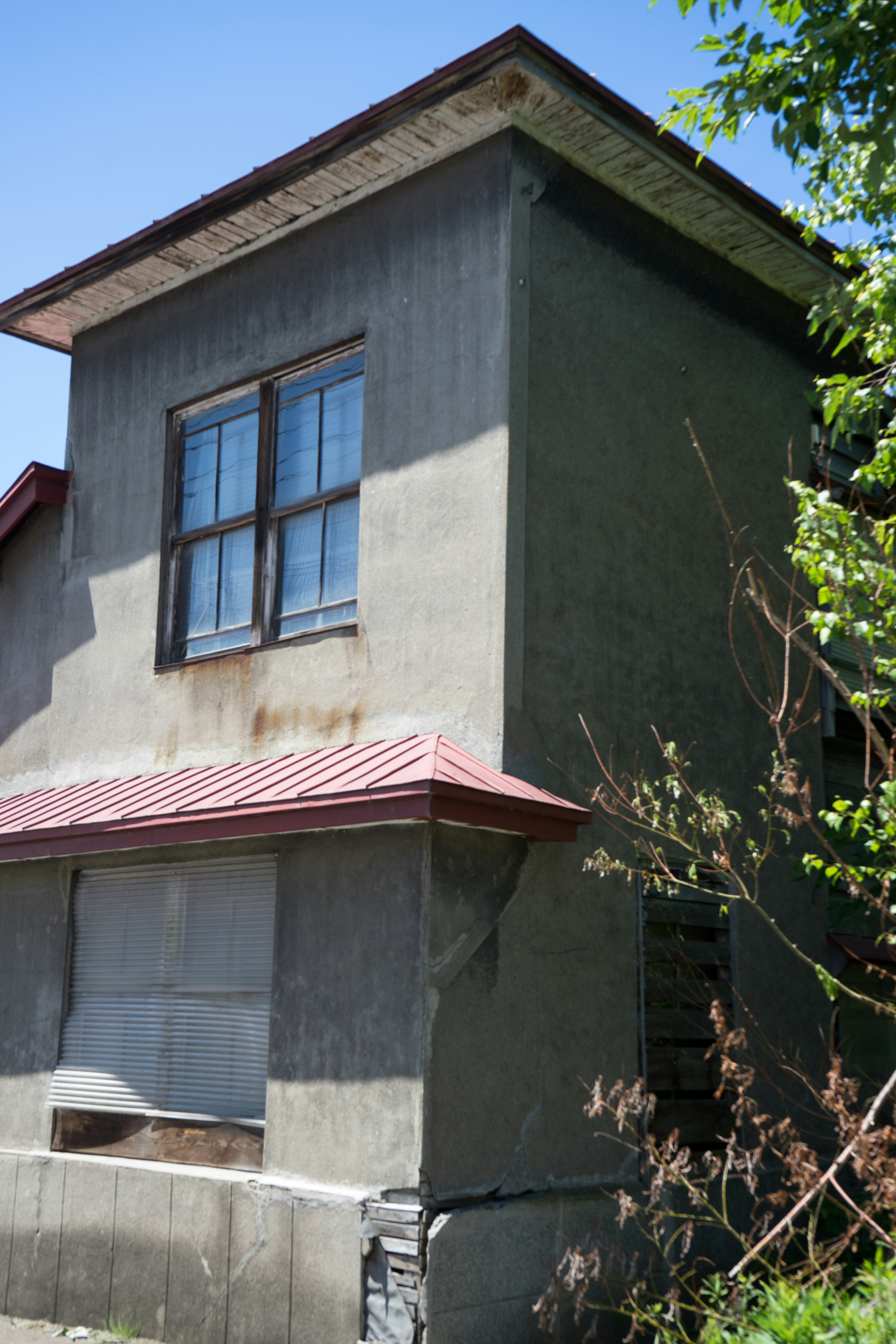 Exterior de una casa antigua con un techo rojo y ventanas distintivas rodeadas de vegetación