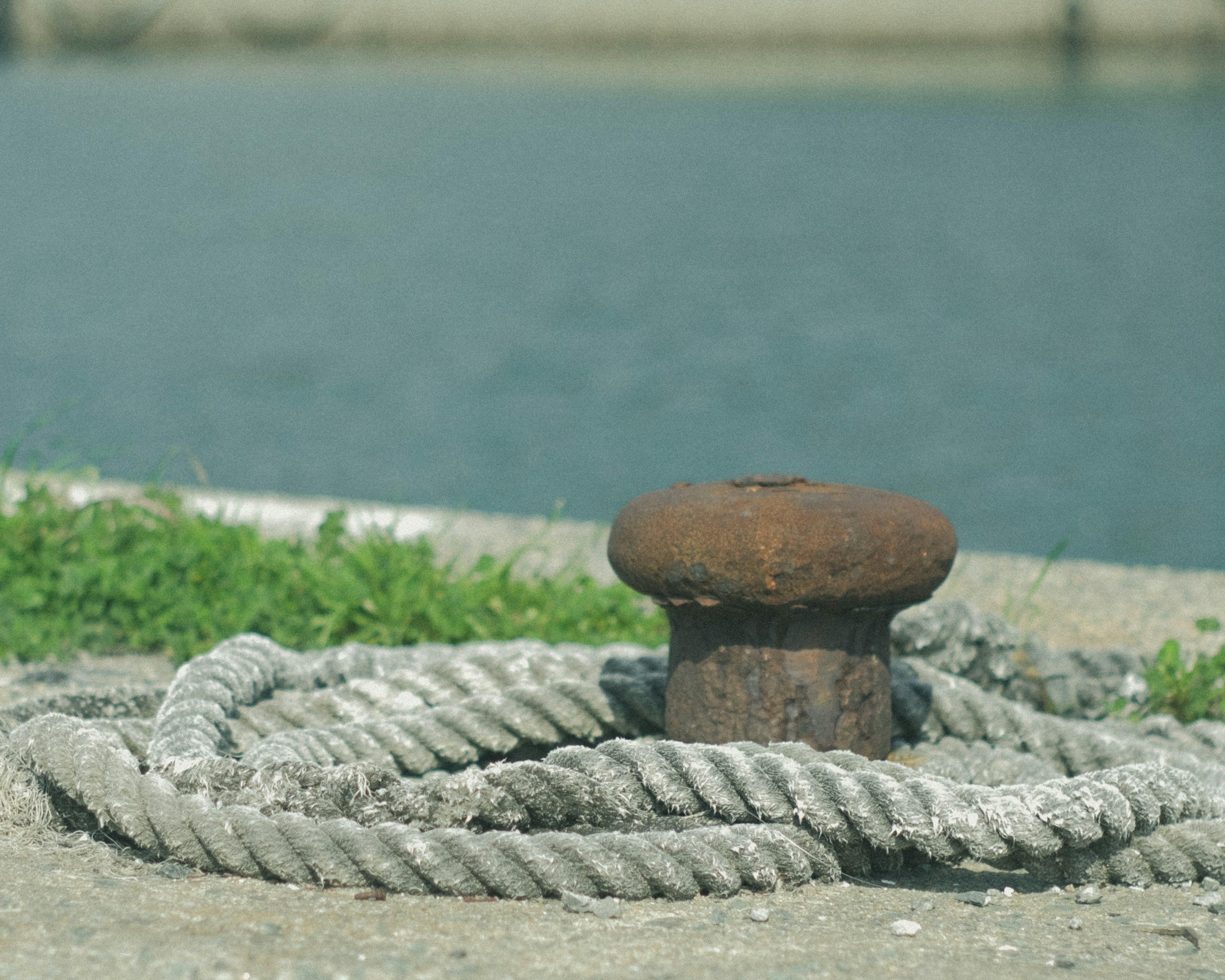 Rusty bollard surrounded by coiled rope and calm water surface