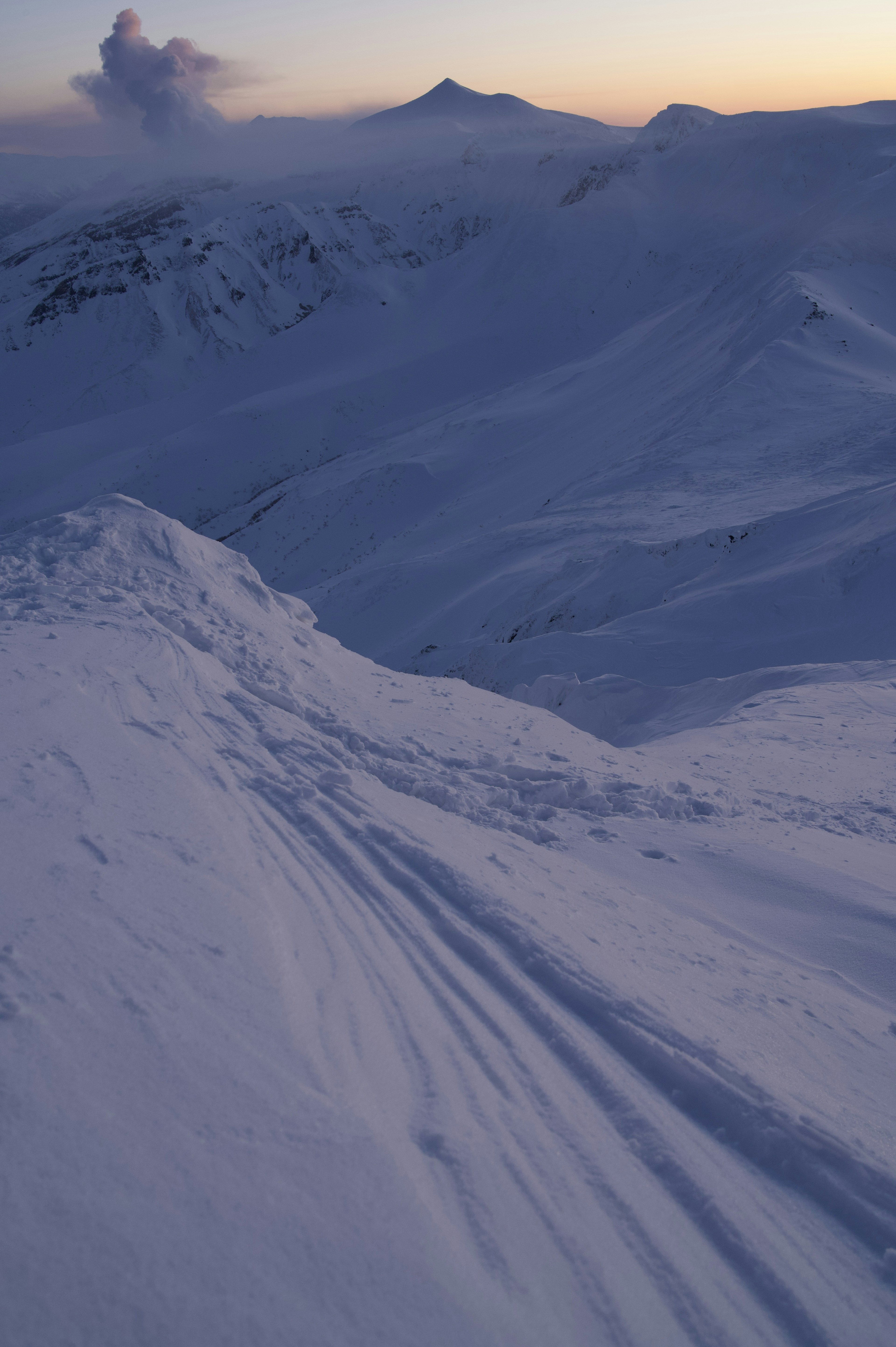 Schneebedeckte Berglandschaft mit Skispuren bei Sonnenuntergang