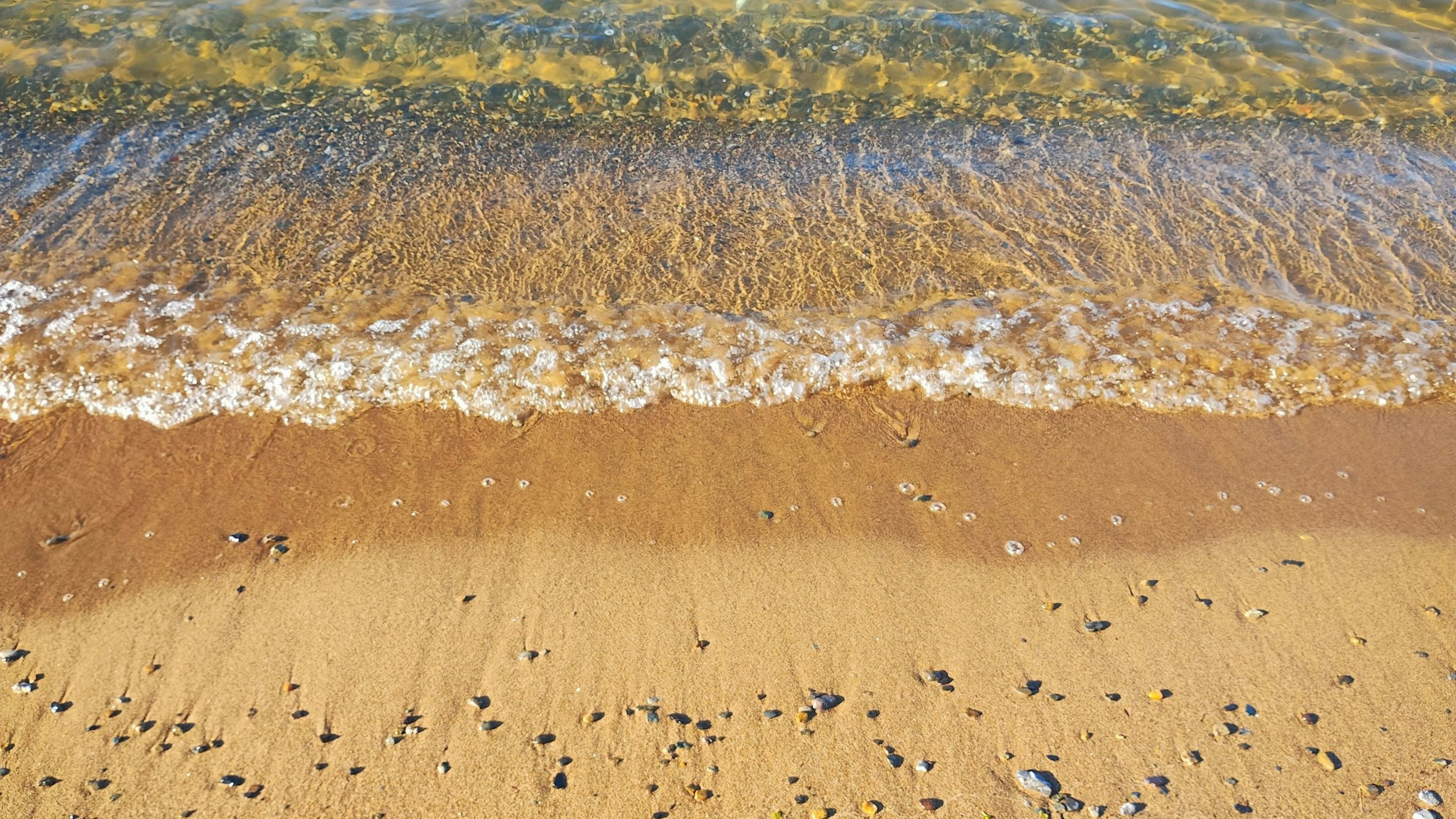 Pemandangan ombak lembut yang menghantam pantai berpasir